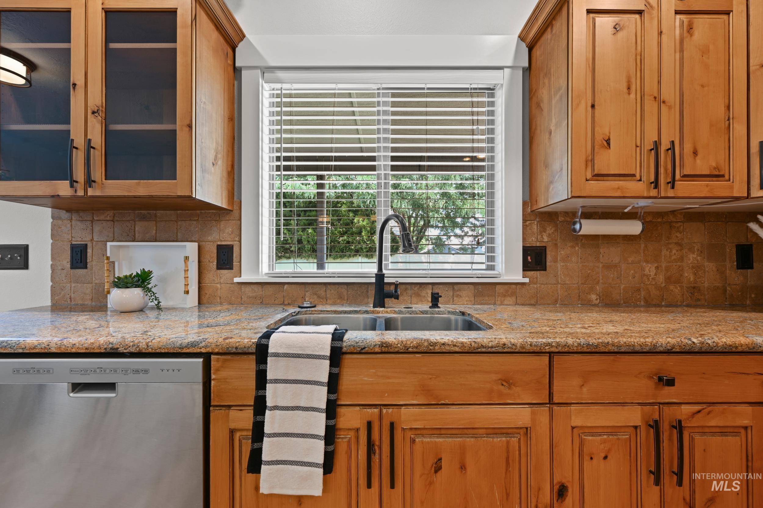 Kitchen featuring dishwasher, light stone counters, decorative backsplash, glass insert cabinets, and brown cabinets