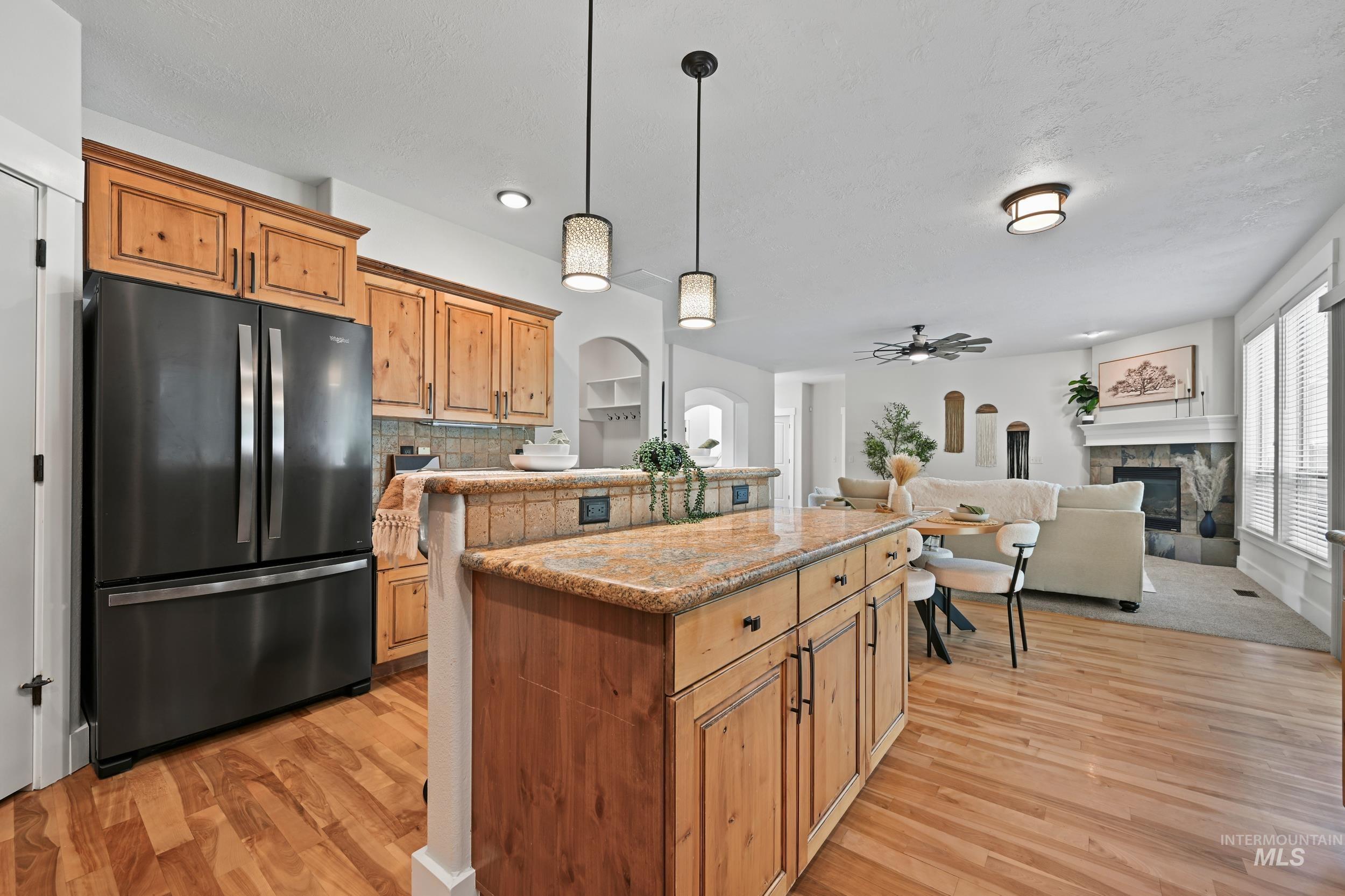Kitchen with hanging light fixtures, arched walkways, freestanding refrigerator, a center island, and a fireplace