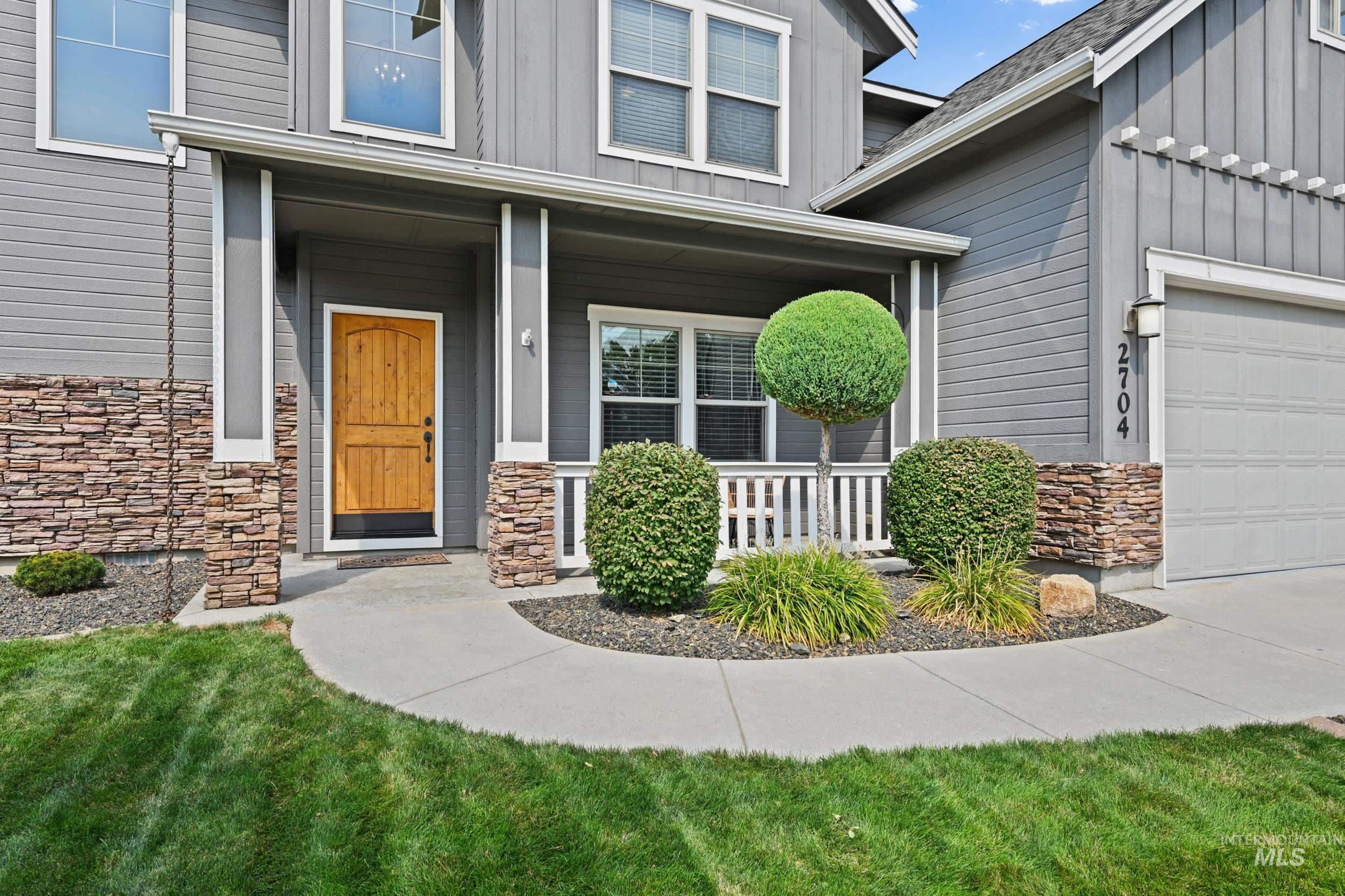 Doorway to property with board and batten siding, stone siding, a porch, a garage, and a yard