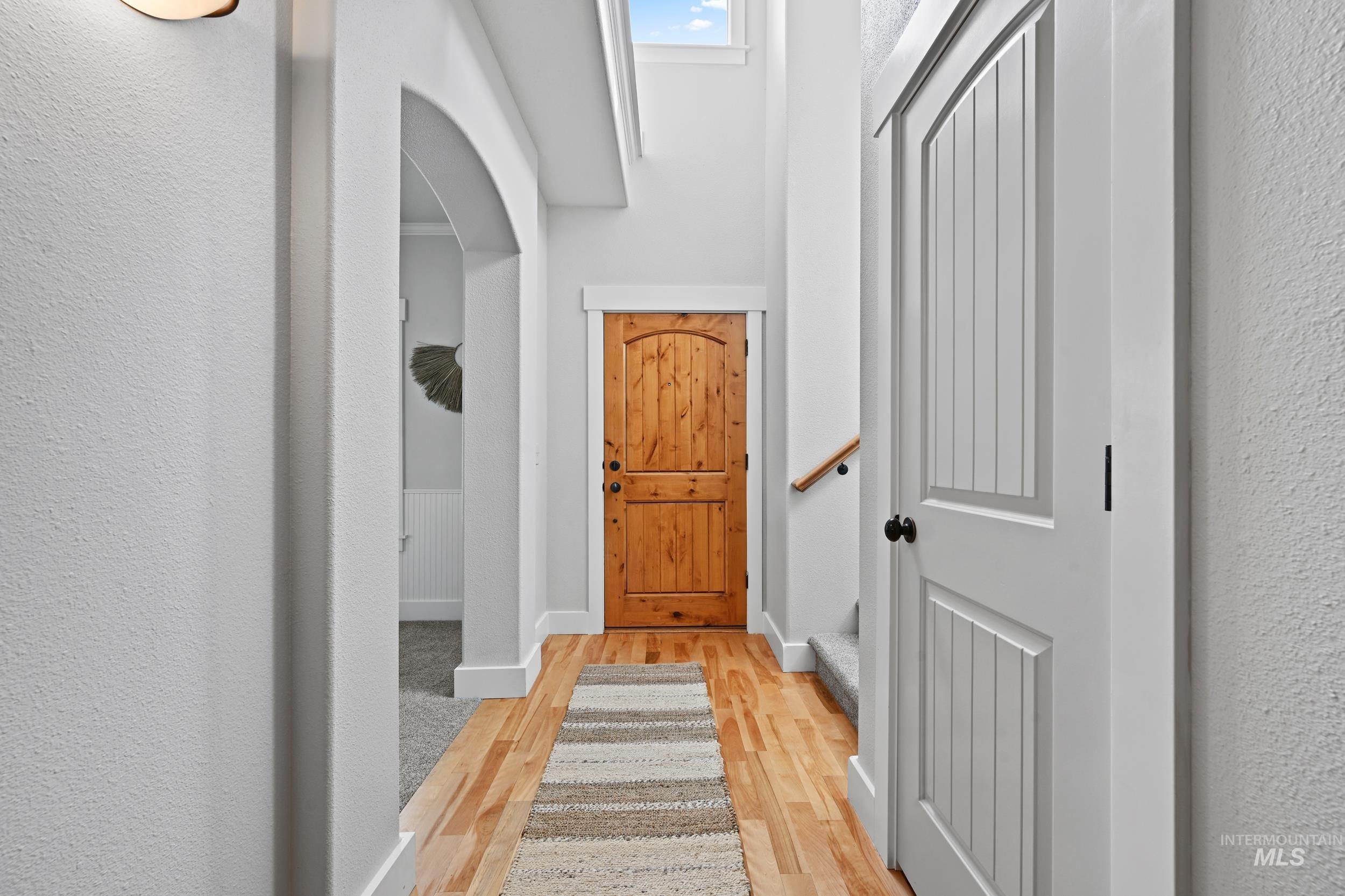 Foyer with light wood-style flooring, arched walkways, a textured wall, and stairway