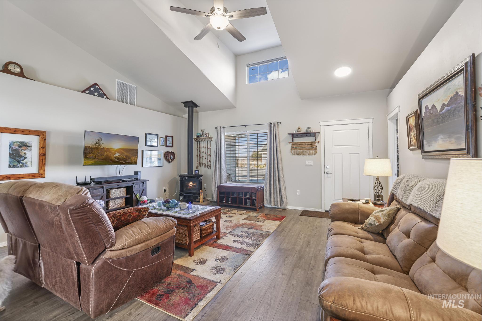 Living area with a wood stove, wood finished floors, a high ceiling, and a ceiling fan