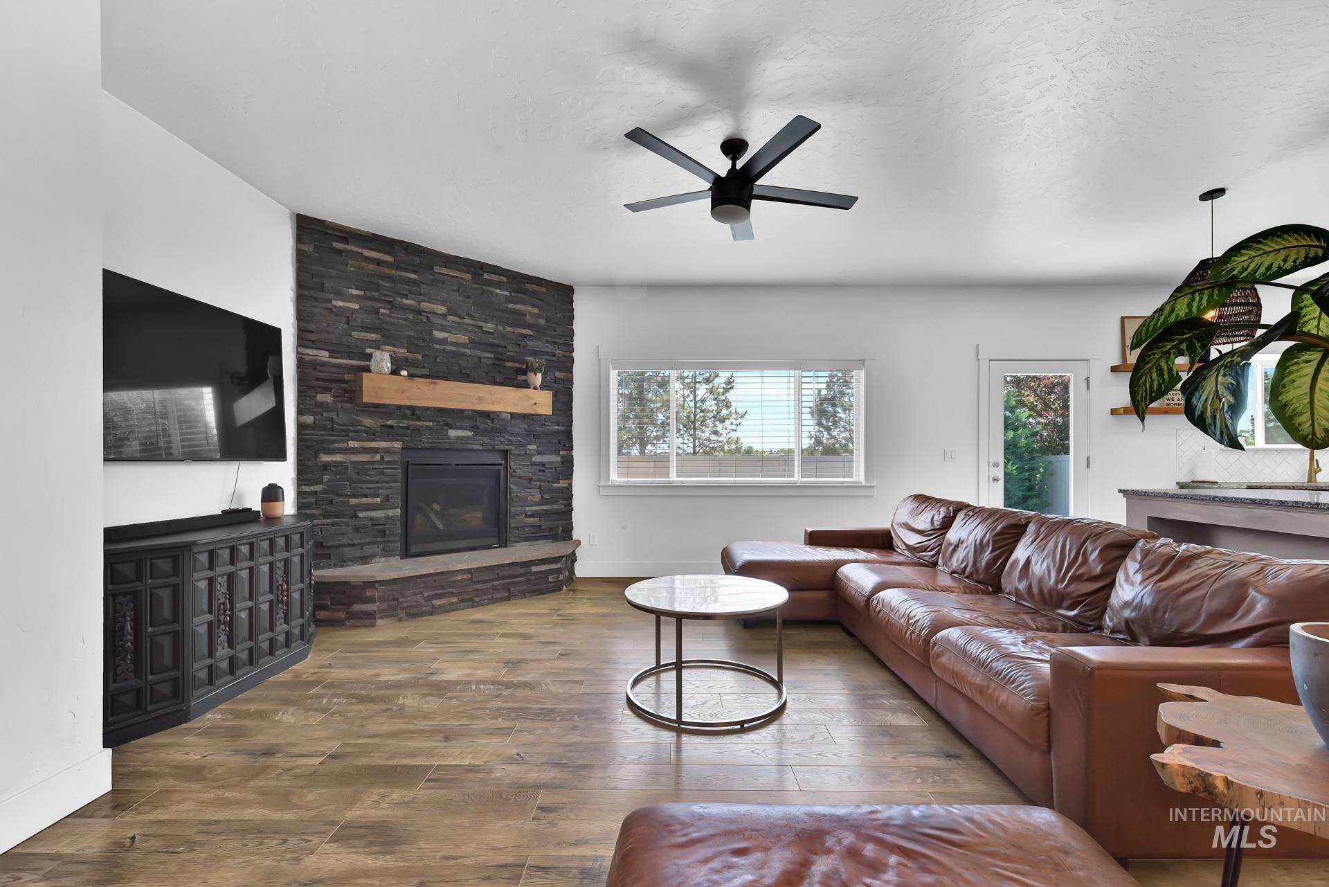 Living area featuring wood finished floors, a fireplace, ceiling fan, and a textured ceiling