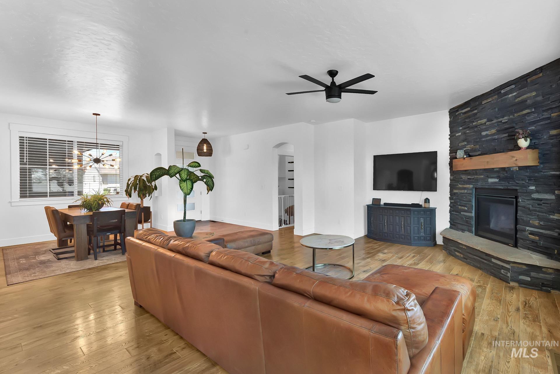 Living area with ceiling fan, a stone fireplace, light wood-style flooring, and arched walkways