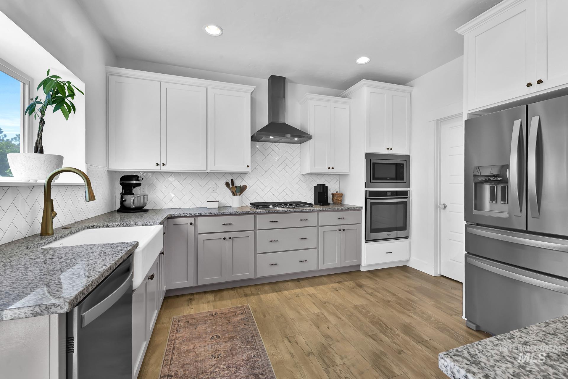 Kitchen with appliances with stainless steel finishes, wall chimney range hood, white cabinetry, backsplash, and light stone countertops