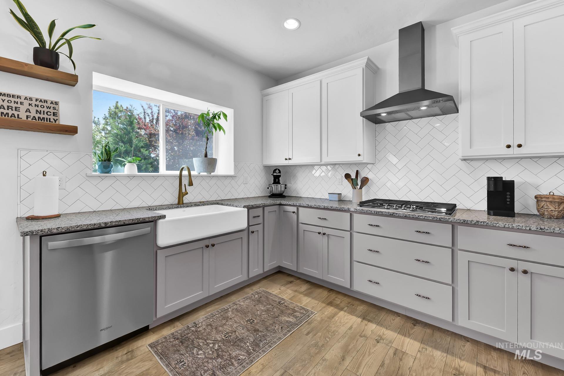 Kitchen with light stone counters, appliances with stainless steel finishes, wall chimney exhaust hood, white cabinets, and recessed lighting