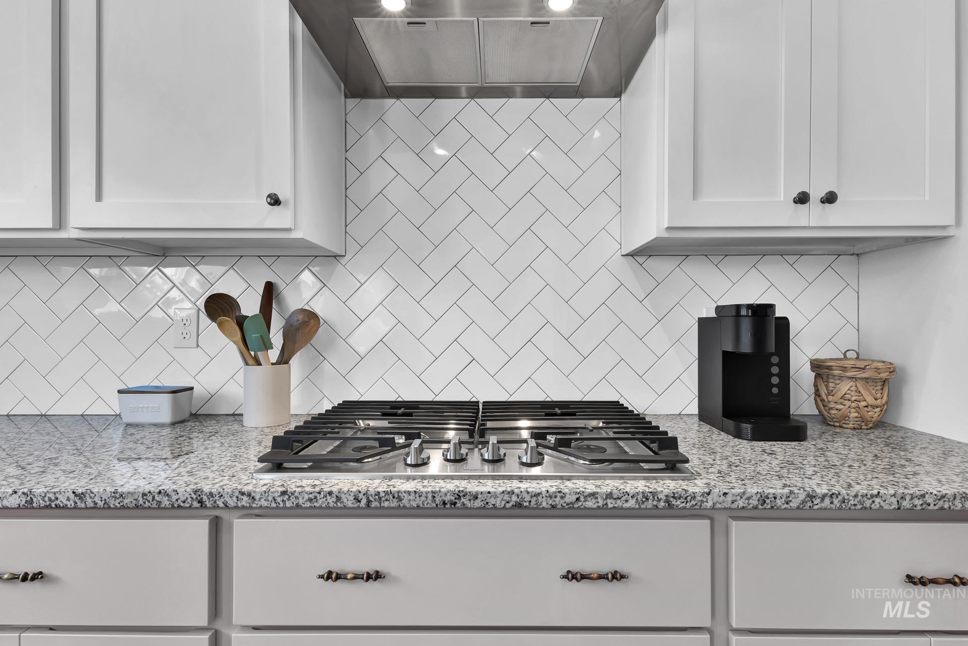 Kitchen featuring light stone countertops, white cabinets, tasteful backsplash, and exhaust hood