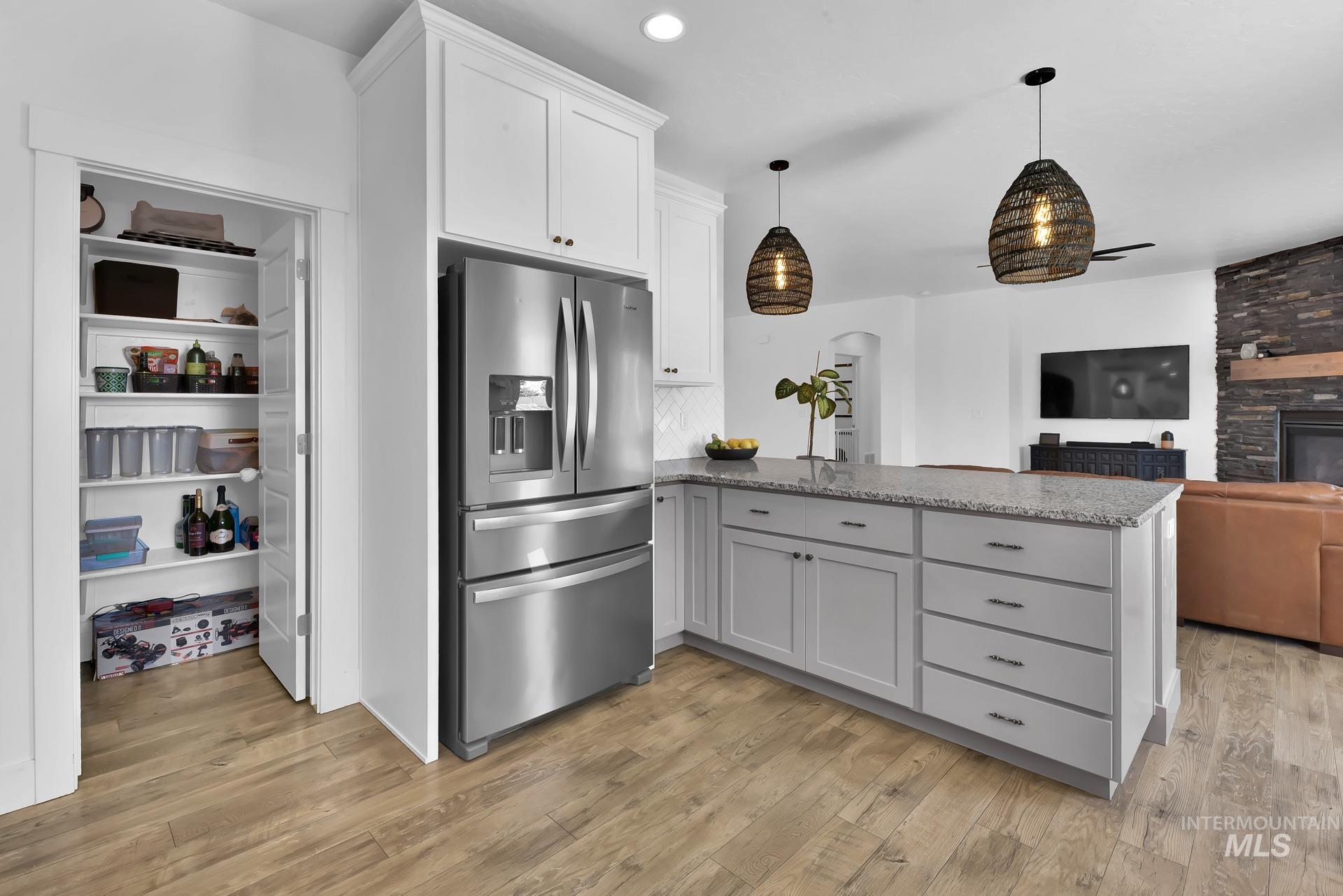 Kitchen featuring stainless steel fridge, a peninsula, hanging light fixtures, white cabinets, and a stone fireplace