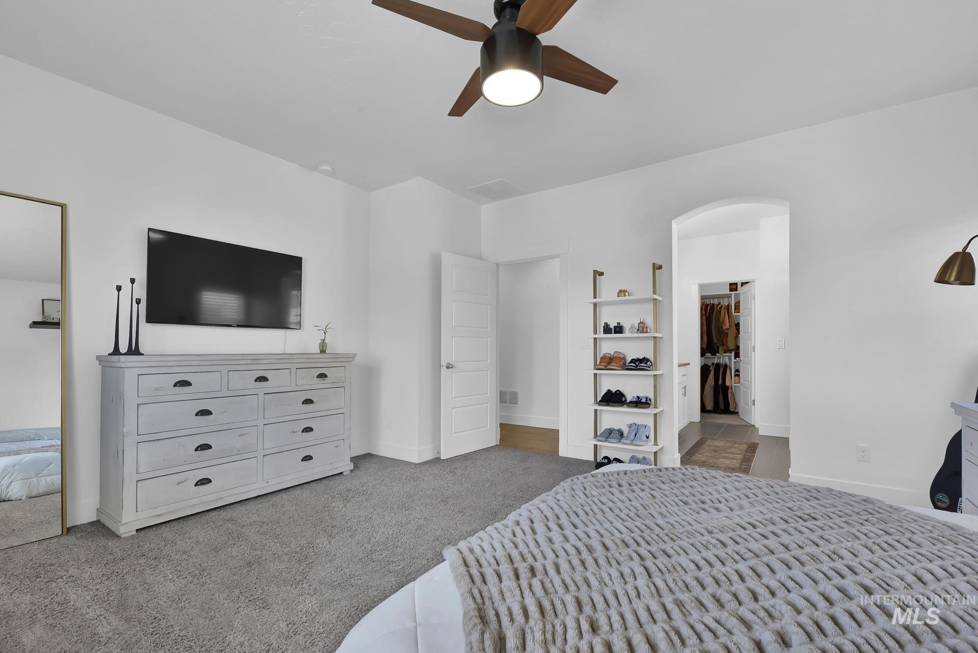 Bedroom with light carpet, ceiling fan, arched walkways, and a walk in closet