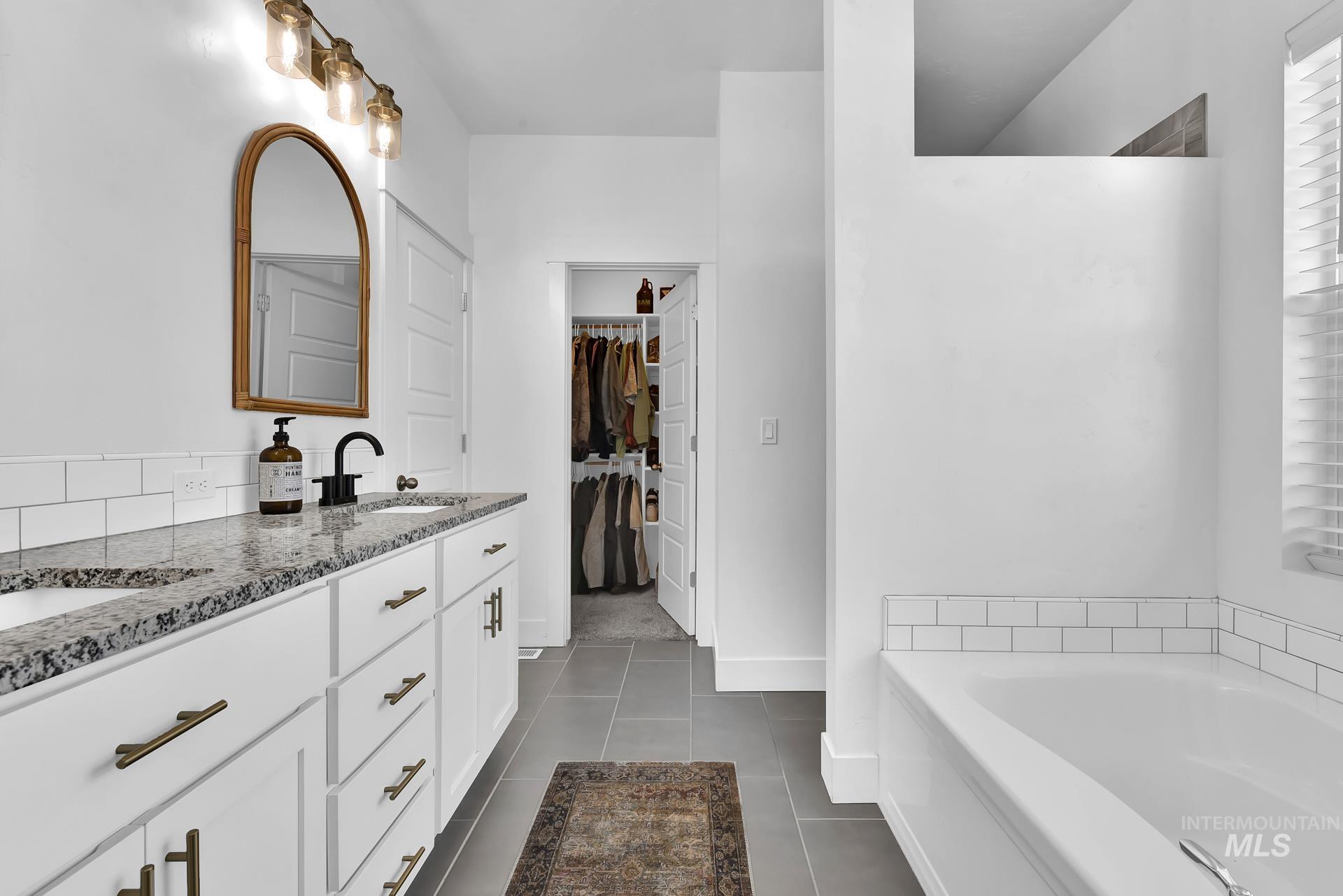Full bathroom with a bath, double vanity, a spacious closet, and dark tile patterned floors