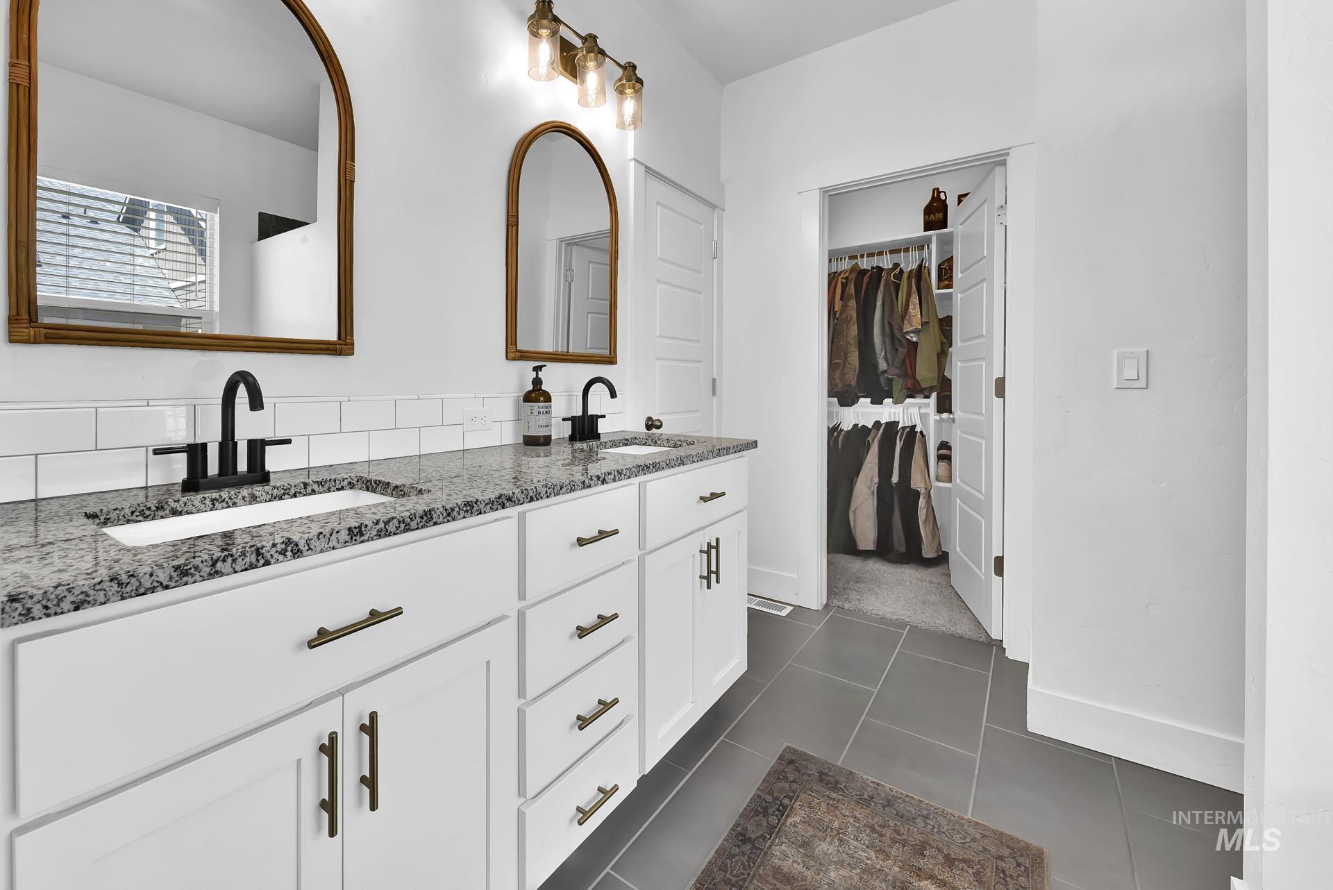 Full bath featuring double vanity, a spacious closet, and dark tile patterned floors