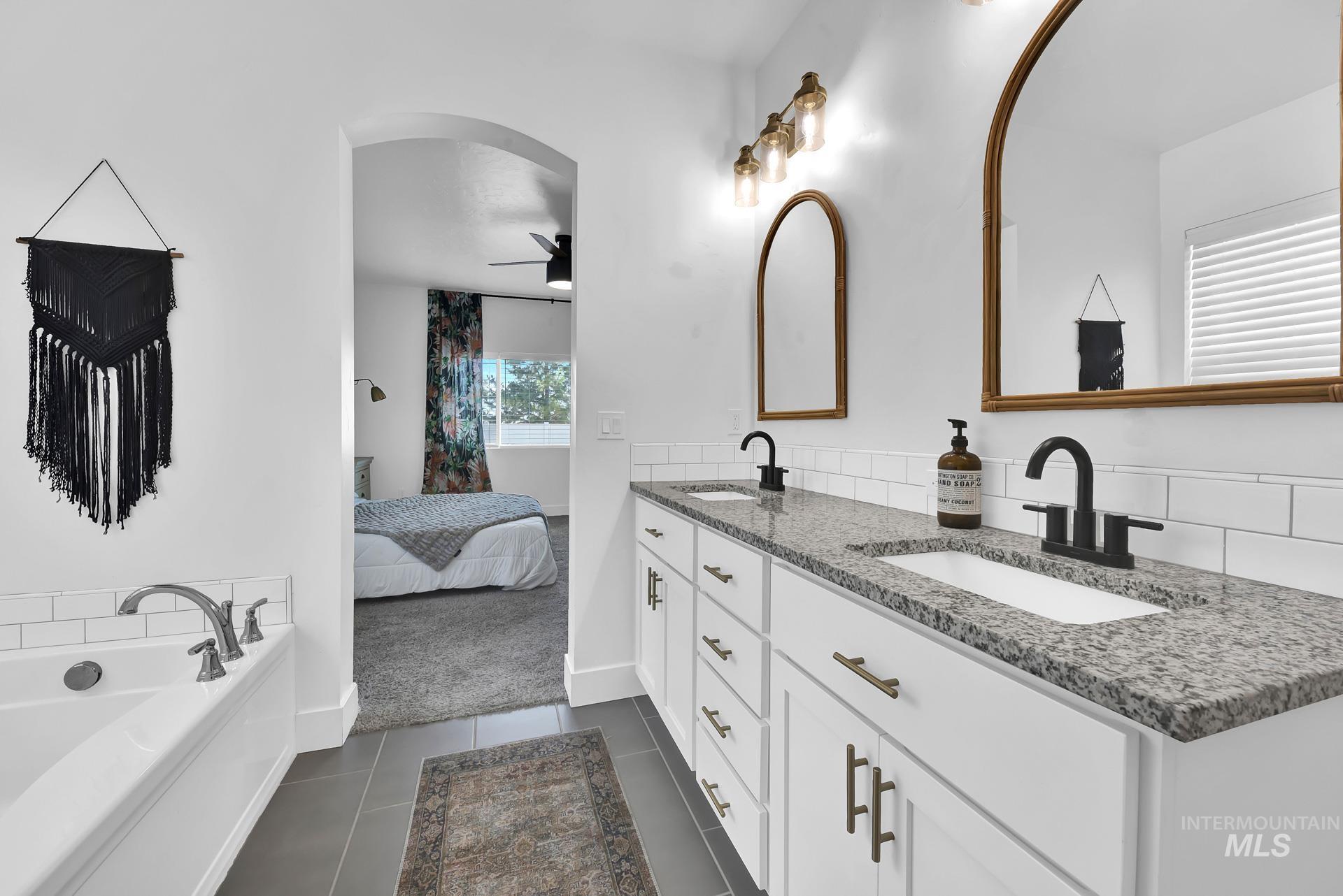 Bathroom with dark tile patterned floors, double vanity, a bath, and ceiling fan