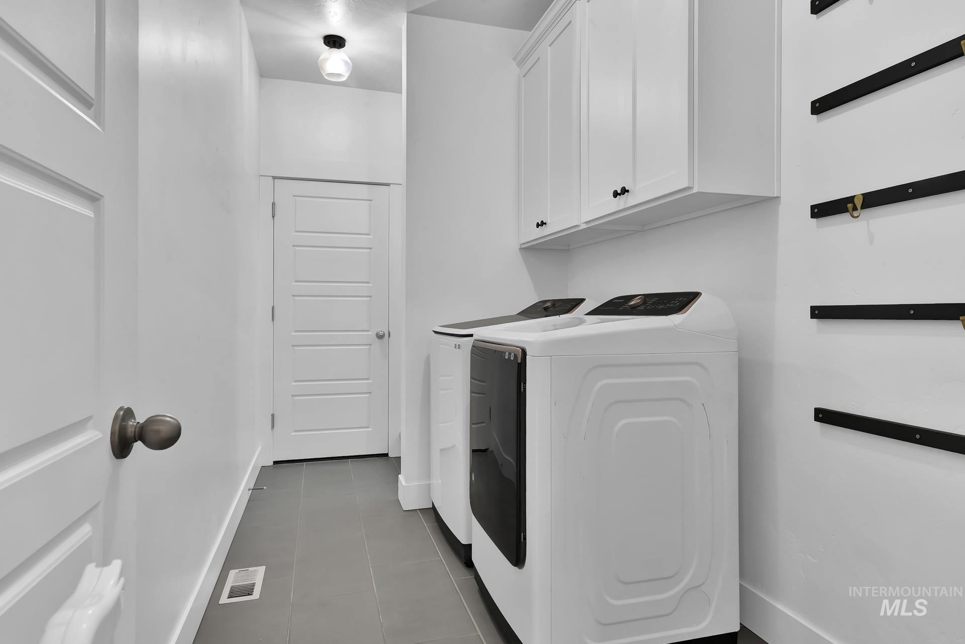 Laundry area with dark tile patterned floors, washer and dryer, and cabinet space