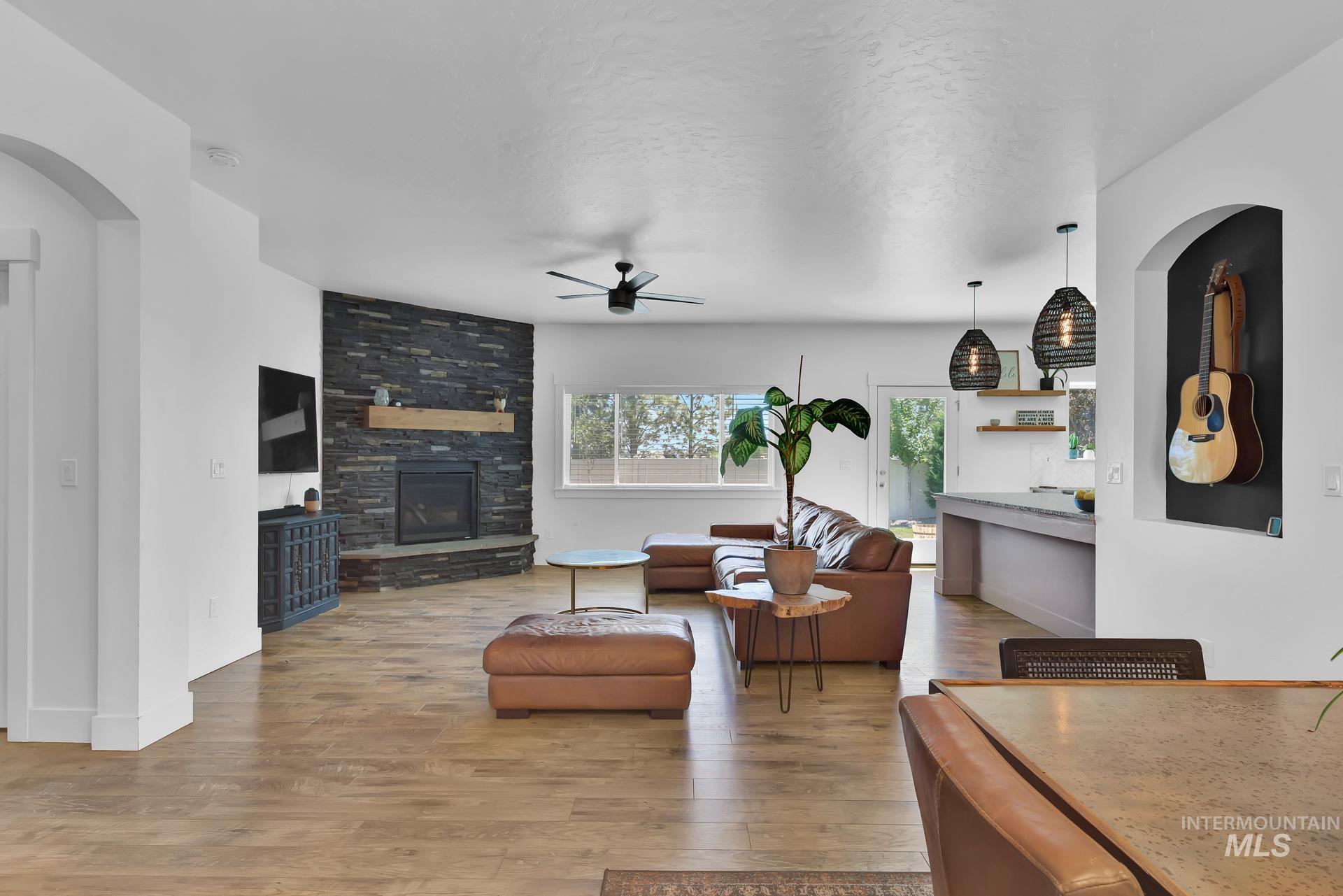 Living room with arched walkways, light wood-style flooring, a stone fireplace, ceiling fan, and a textured ceiling