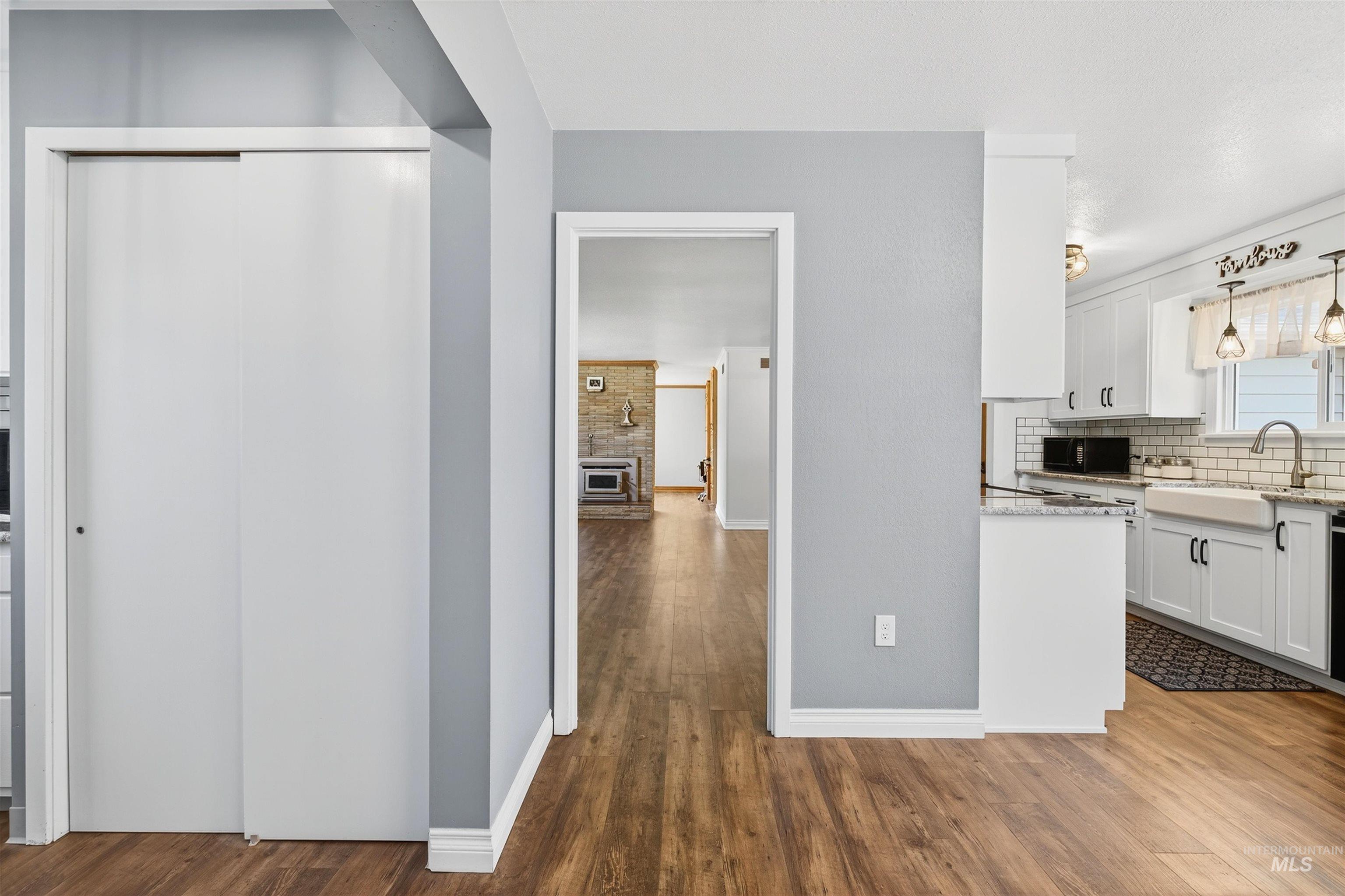 Kitchen featuring white cabinets, backsplash, light stone countertops, dark wood-style flooring, and black microwave
