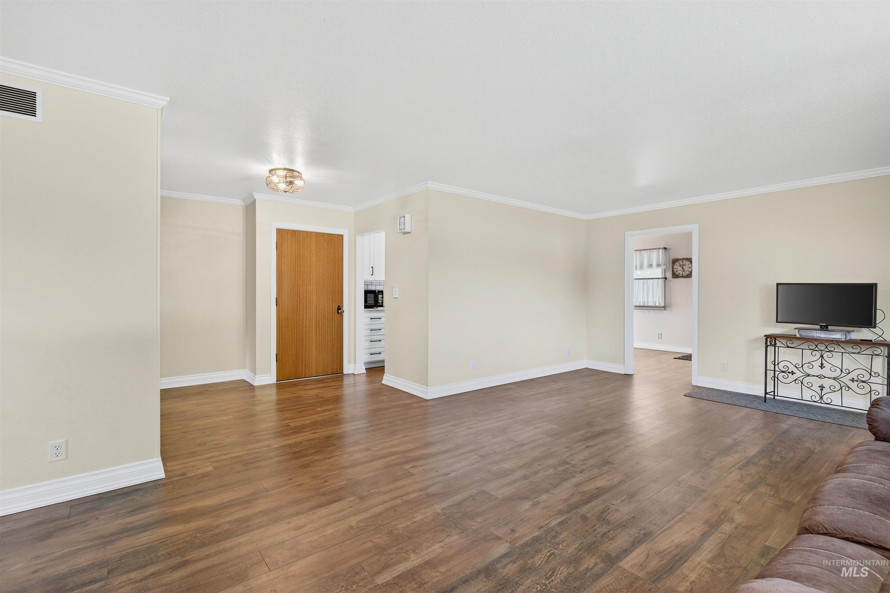 Unfurnished living room with dark wood-style flooring and crown molding