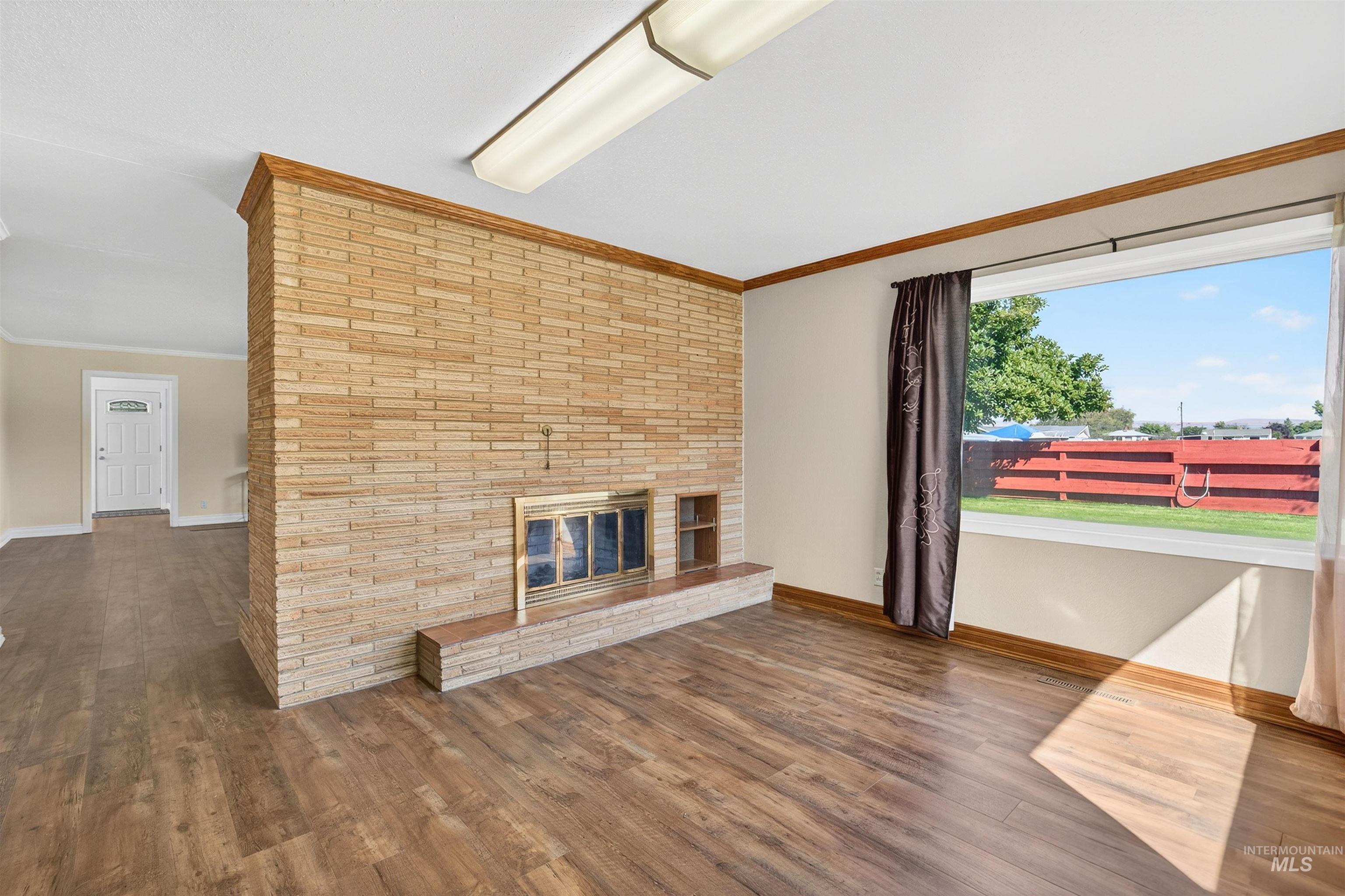 Unfurnished living room featuring a brick fireplace, dark wood-type flooring, and ornamental molding