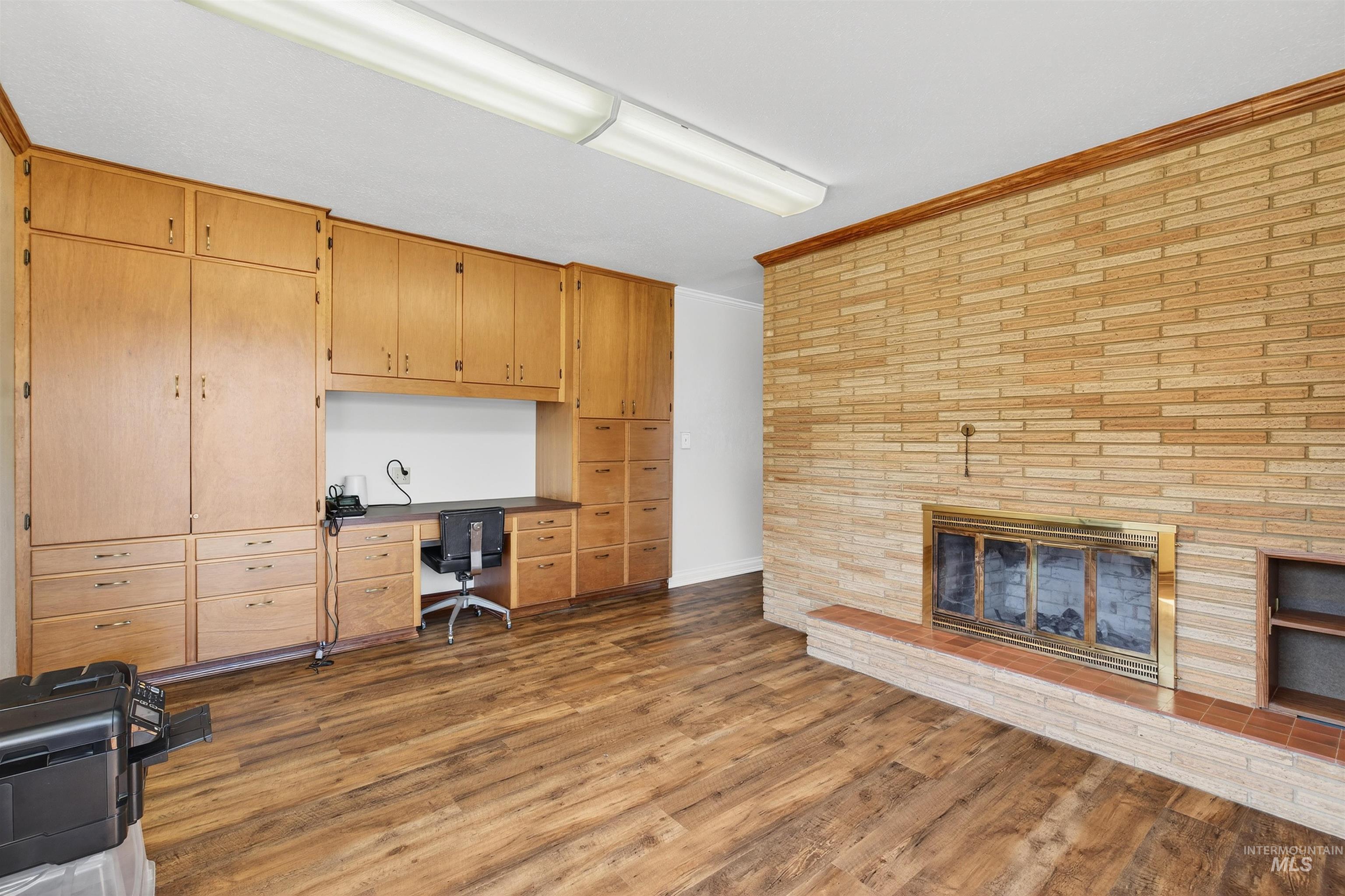 Office with dark wood-style flooring, crown molding, a brick fireplace, and built in desk