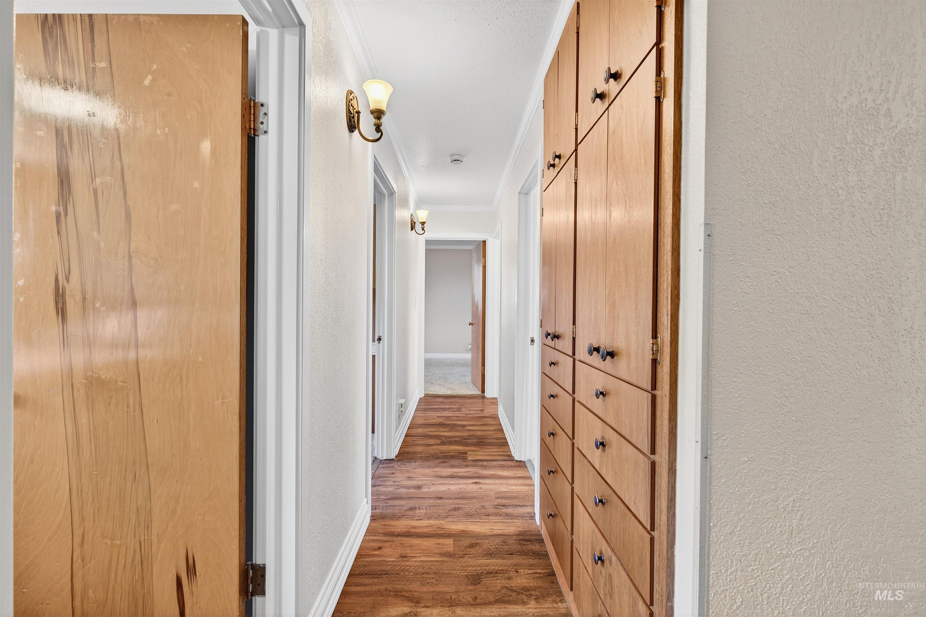 Corridor featuring light wood-style flooring, a textured wall, and crown molding