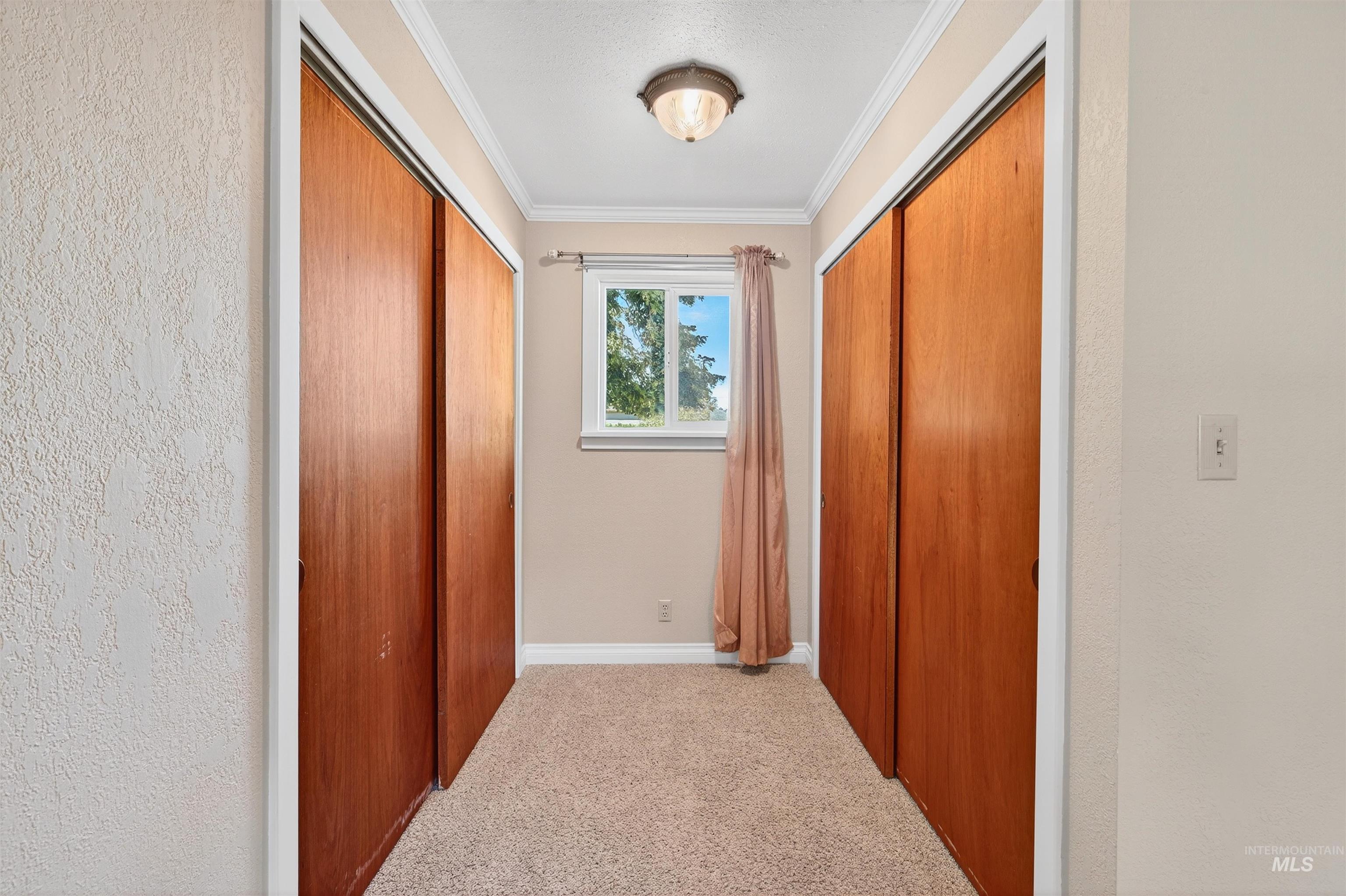 Corridor featuring crown molding, light colored carpet, and a textured wall