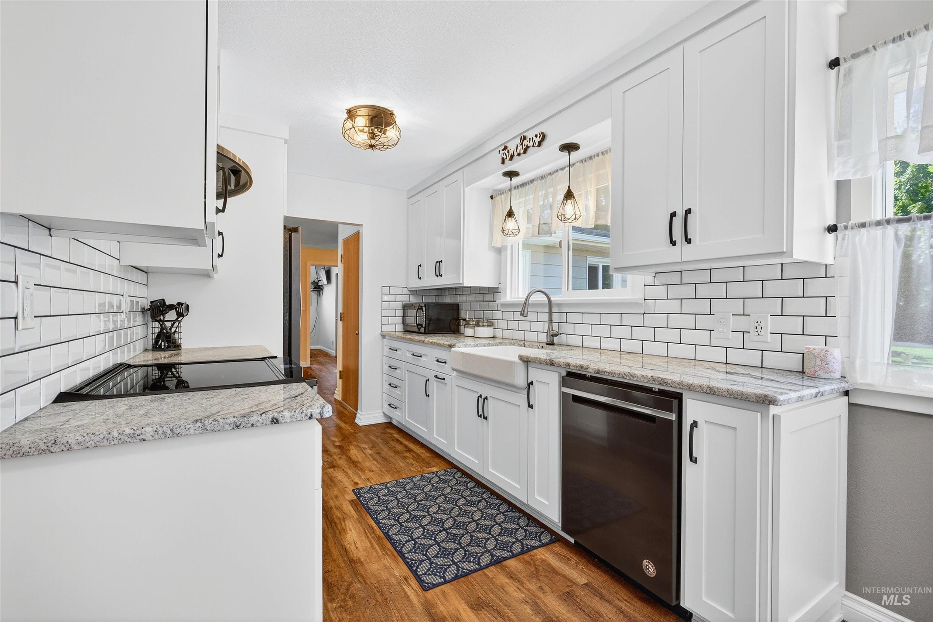 Kitchen with light stone counters, white cabinets, dark wood-type flooring, and dishwasher