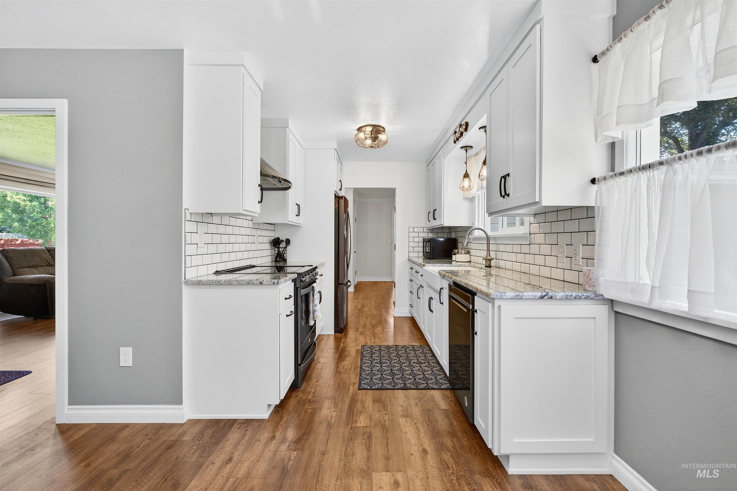 Kitchen featuring light stone countertops, white cabinets, black appliances, and light wood-style flooring