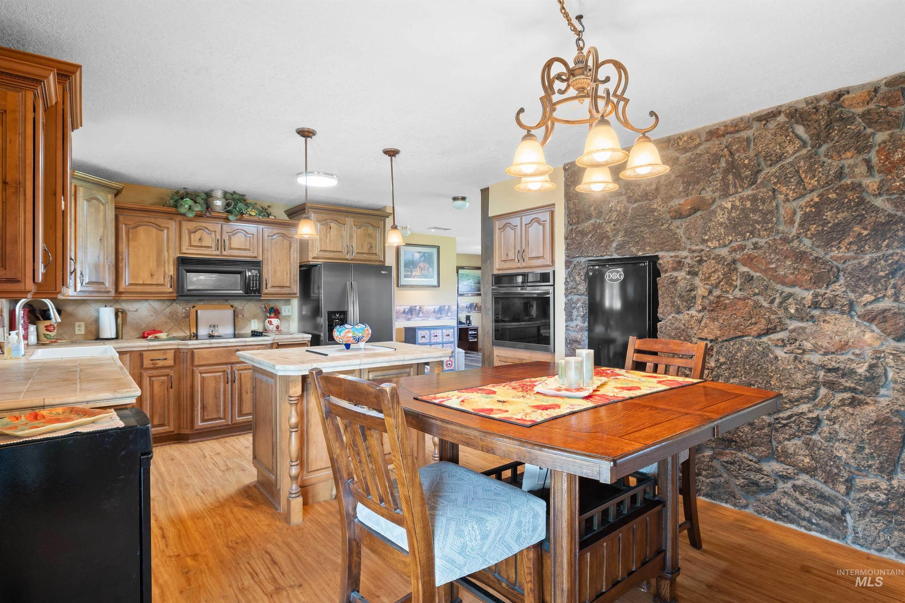 Kitchen featuring brown cabinets, decorative light fixtures, light wood-type flooring, black appliances, and a center island