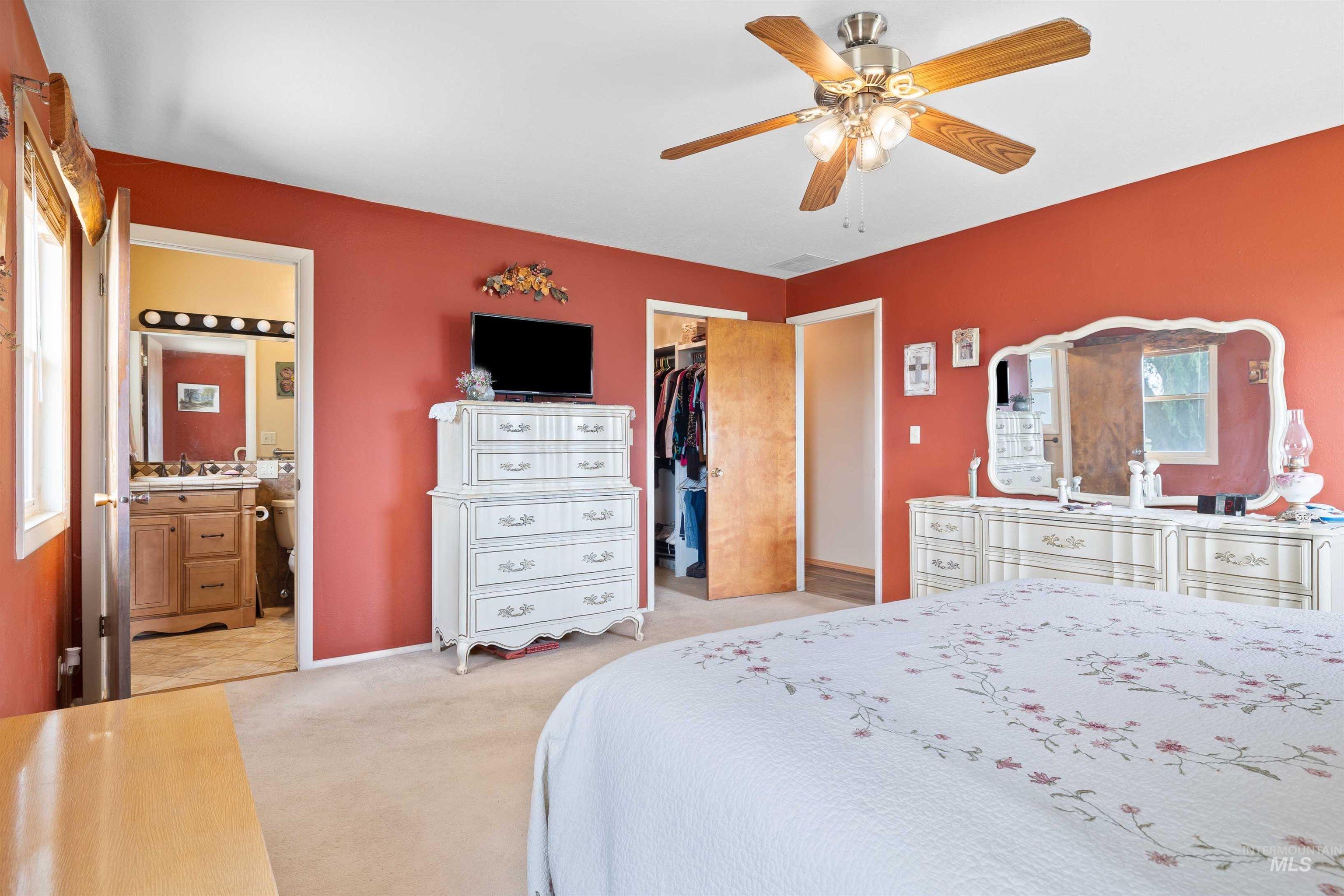 Bedroom with light colored carpet, ensuite bath, a walk in closet, and ceiling fan