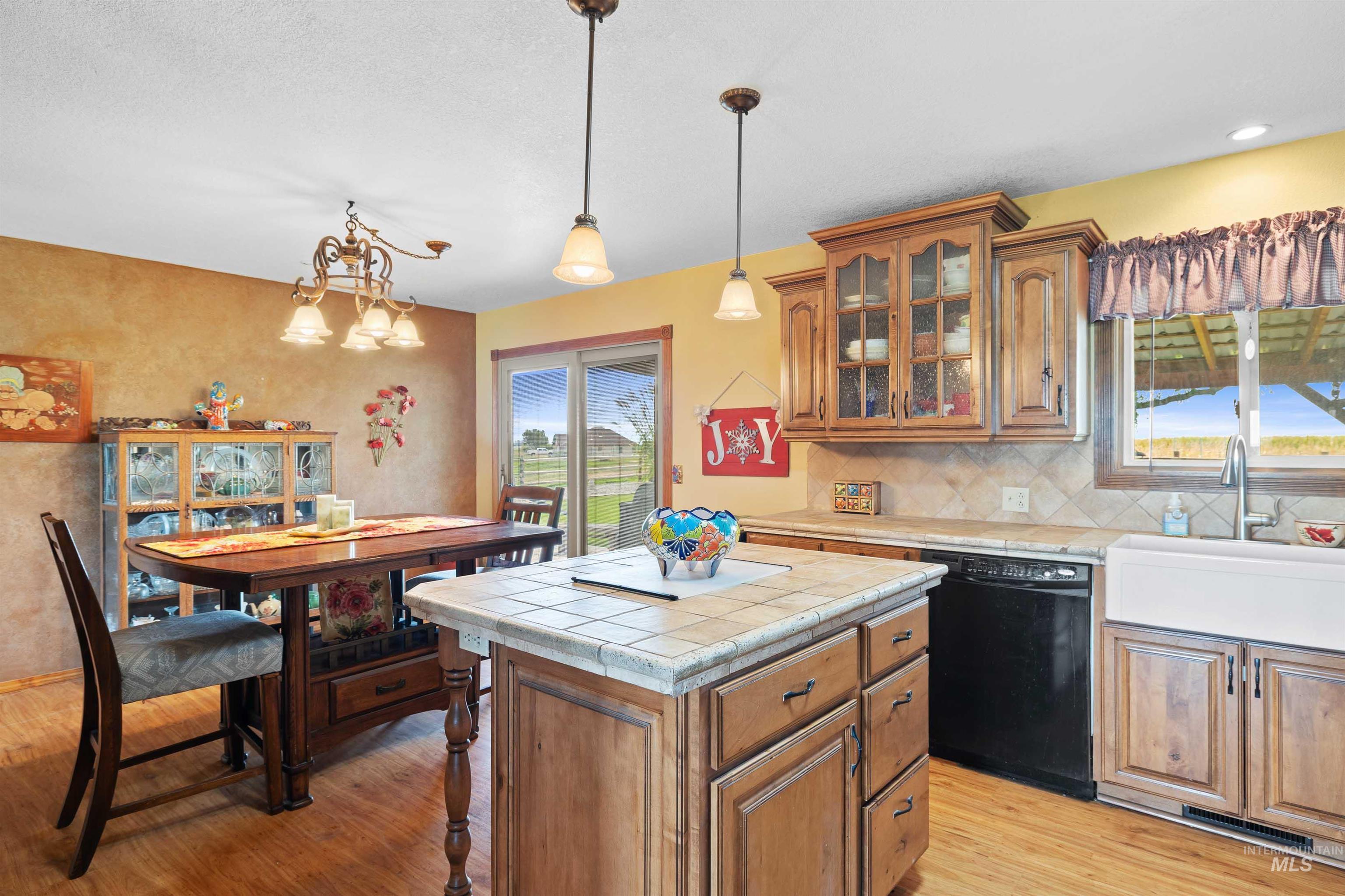 Kitchen featuring brown cabinetry, light wood finished floors, black dishwasher, decorative light fixtures, and tasteful backsplash