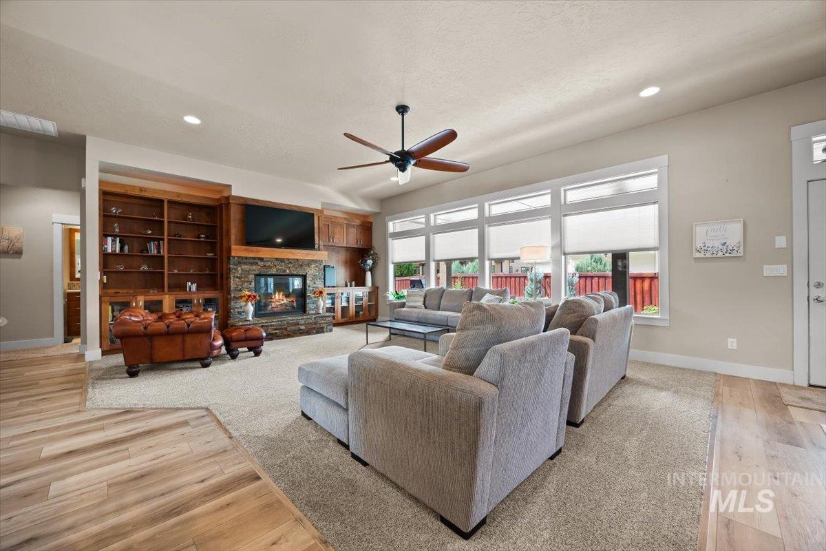 Living room with ceiling fan, a stone fireplace, light wood-style flooring, a textured ceiling, and recessed lighting