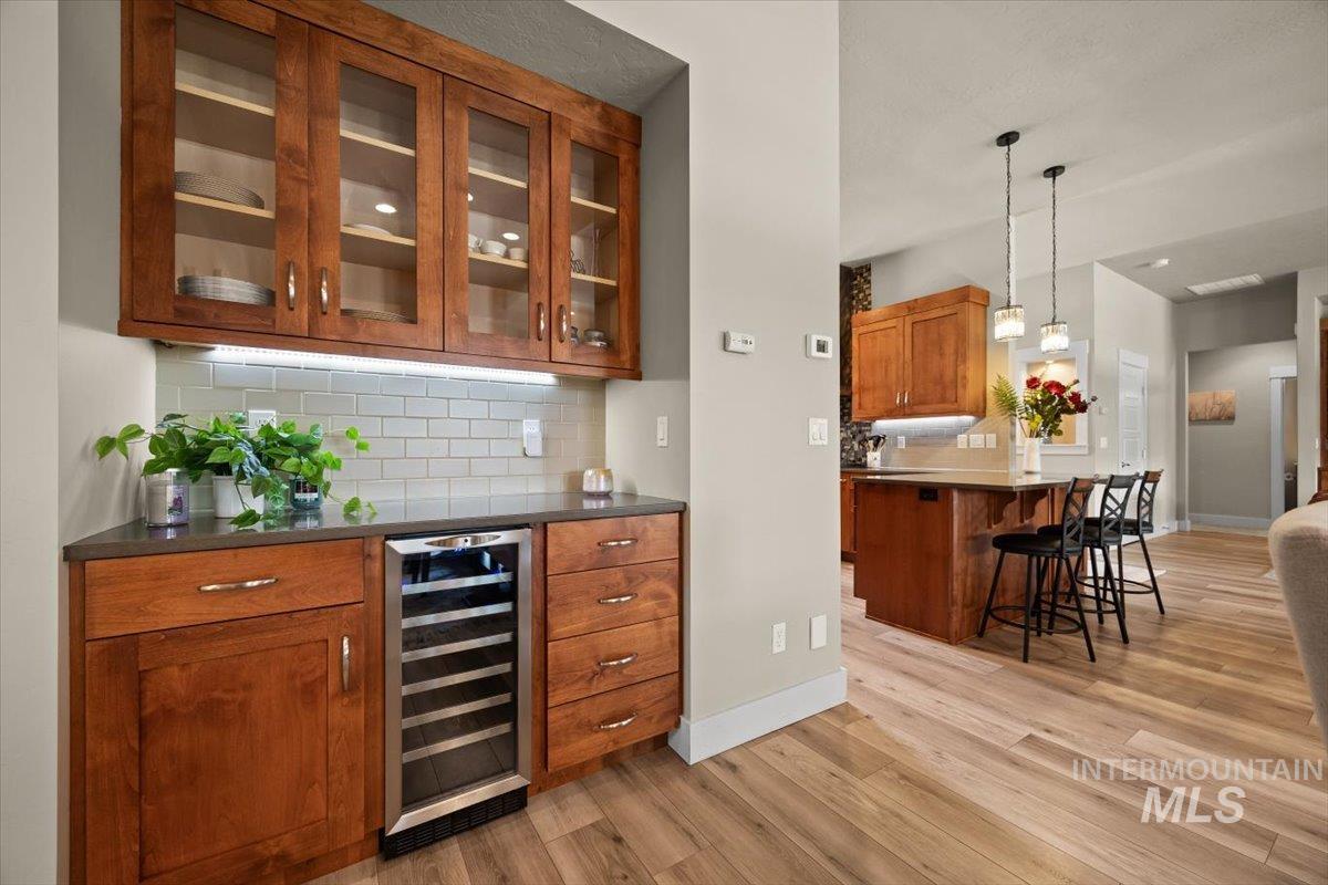Bar featuring brown cabinets, decorative backsplash, wine cooler, and pendant lighting