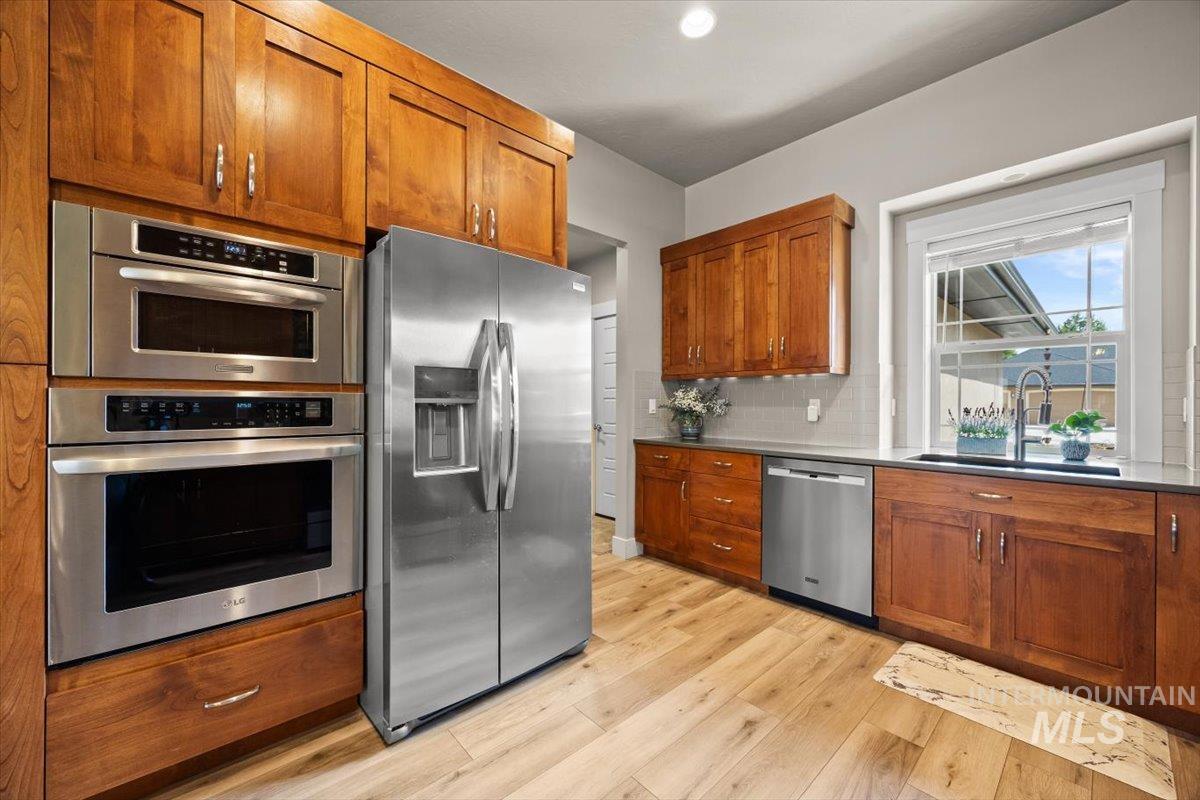 Kitchen with appliances with stainless steel finishes, brown cabinets, light wood-style floors, and backsplash
