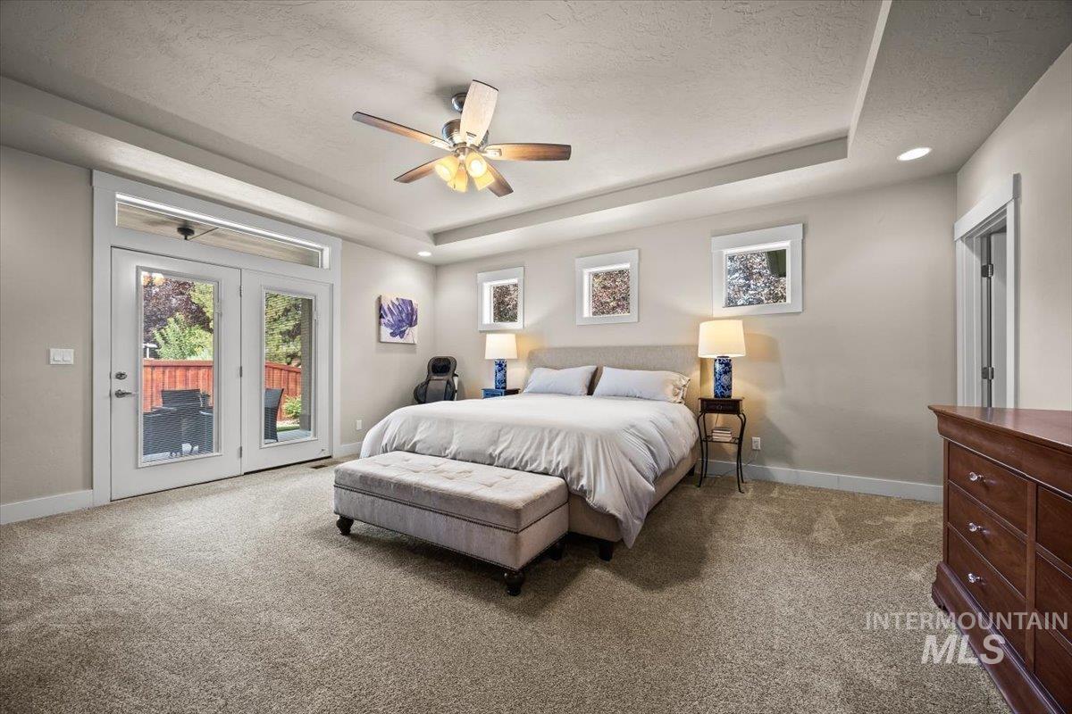 Bedroom with a tray ceiling, light colored carpet, access to exterior, and a textured ceiling