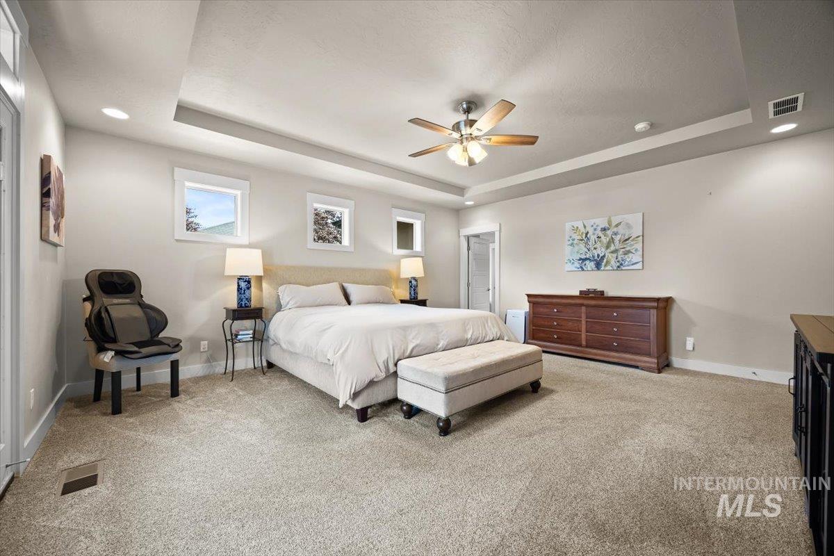 Bedroom with a tray ceiling, light colored carpet, ceiling fan, and recessed lighting