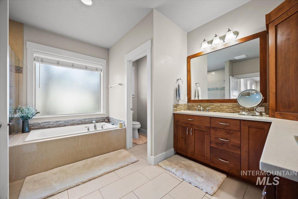 Bathroom with vanity, a bath, backsplash, and light tile patterned flooring