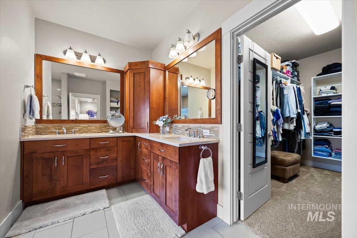 Bathroom with backsplash, double vanity, light tile patterned floors, and a spacious closet