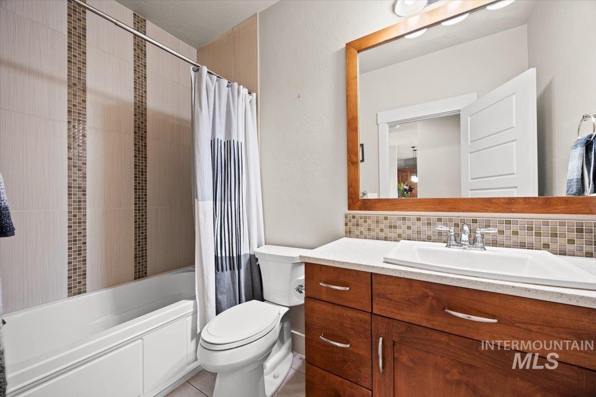 Bathroom with shower / tub combo, vanity, backsplash, and light tile patterned floors
