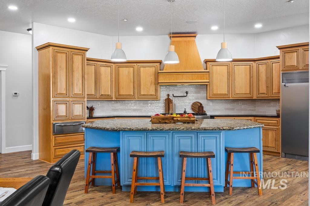 Kitchen with a kitchen bar, built in refrigerator, tasteful backsplash, dark stone counters, and blue cabinetry