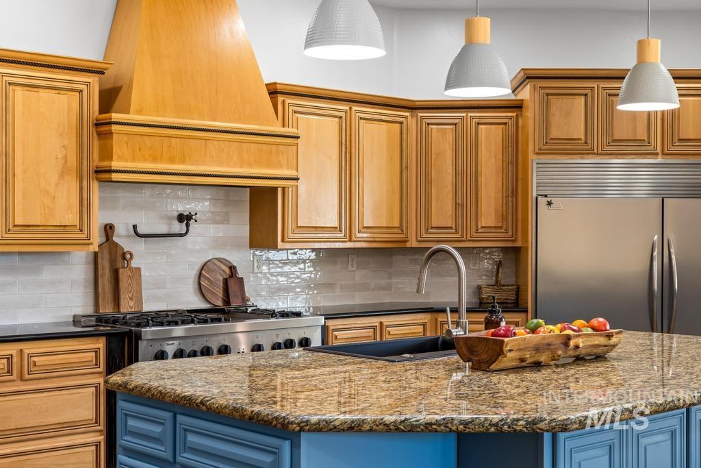 Kitchen featuring dark stone counters, decorative backsplash, built in refrigerator, and premium range hood