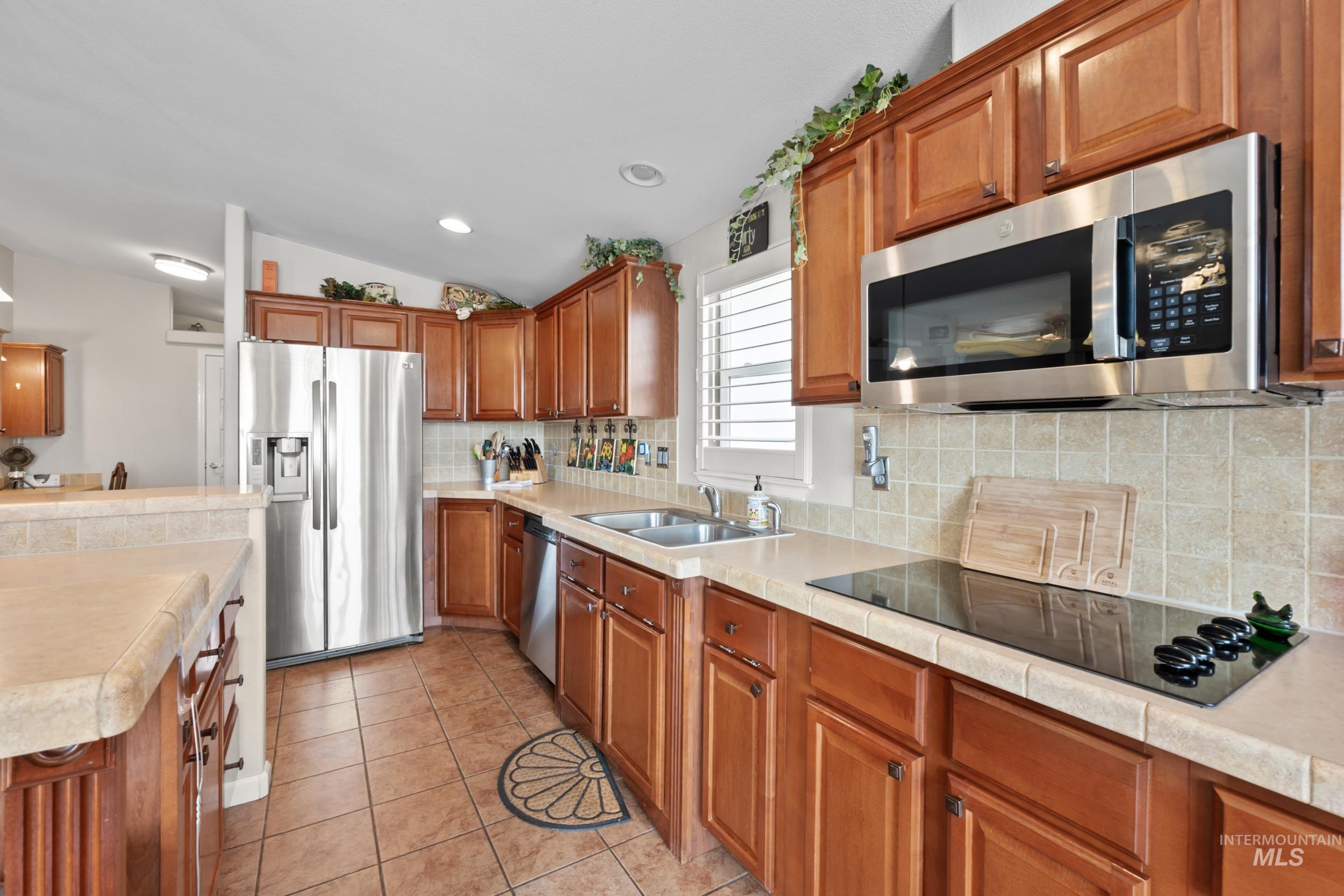 Kitchen featuring stainless steel appliances, brown cabinets, light tile patterned floors, decorative backsplash, and recessed lighting