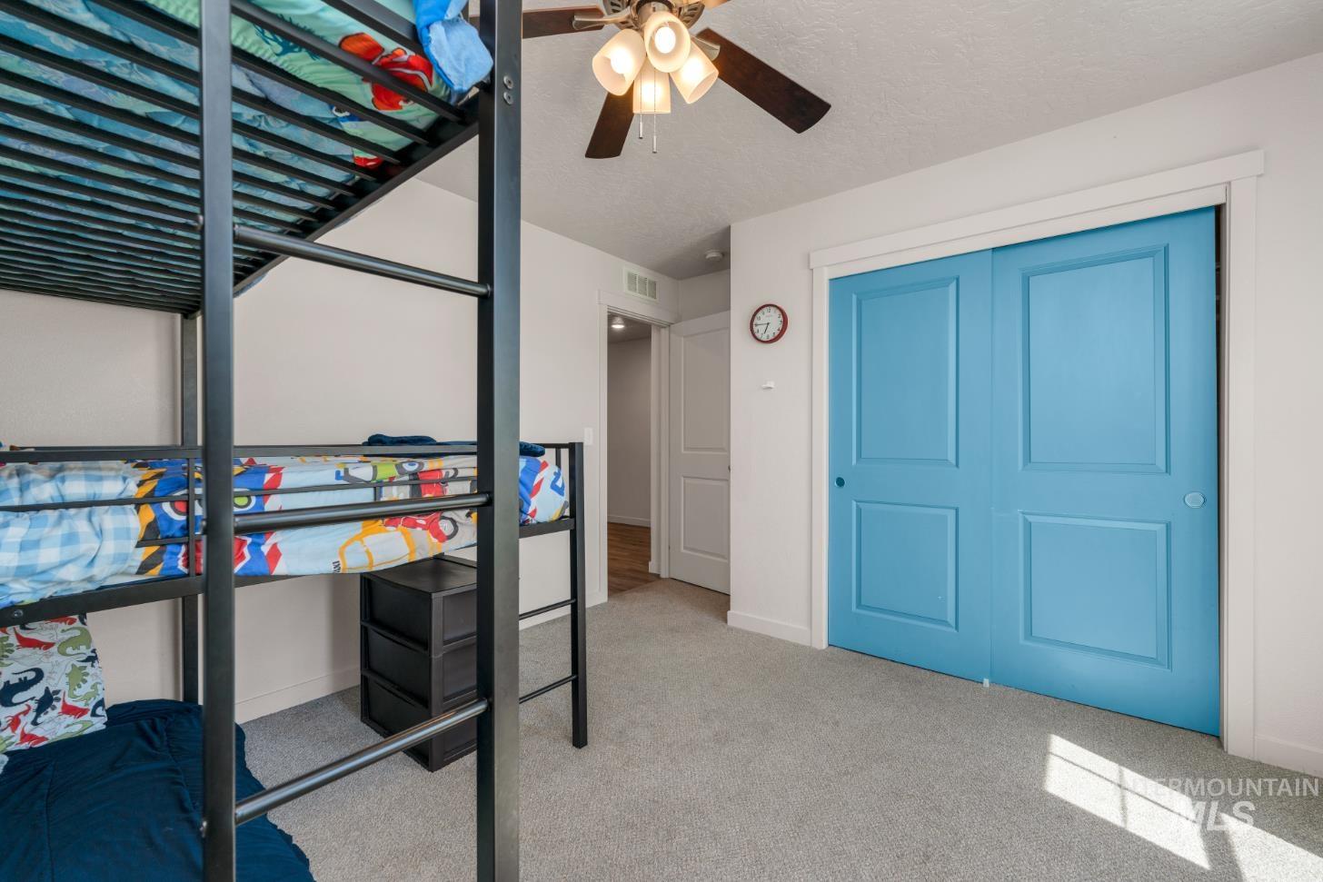 Bedroom with light carpet, a ceiling fan, a textured ceiling, and a closet