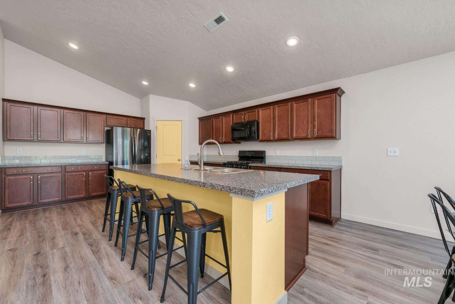 Kitchen featuring a large island with sink, vaulted ceiling, recessed lighting, extra bank of cabinets