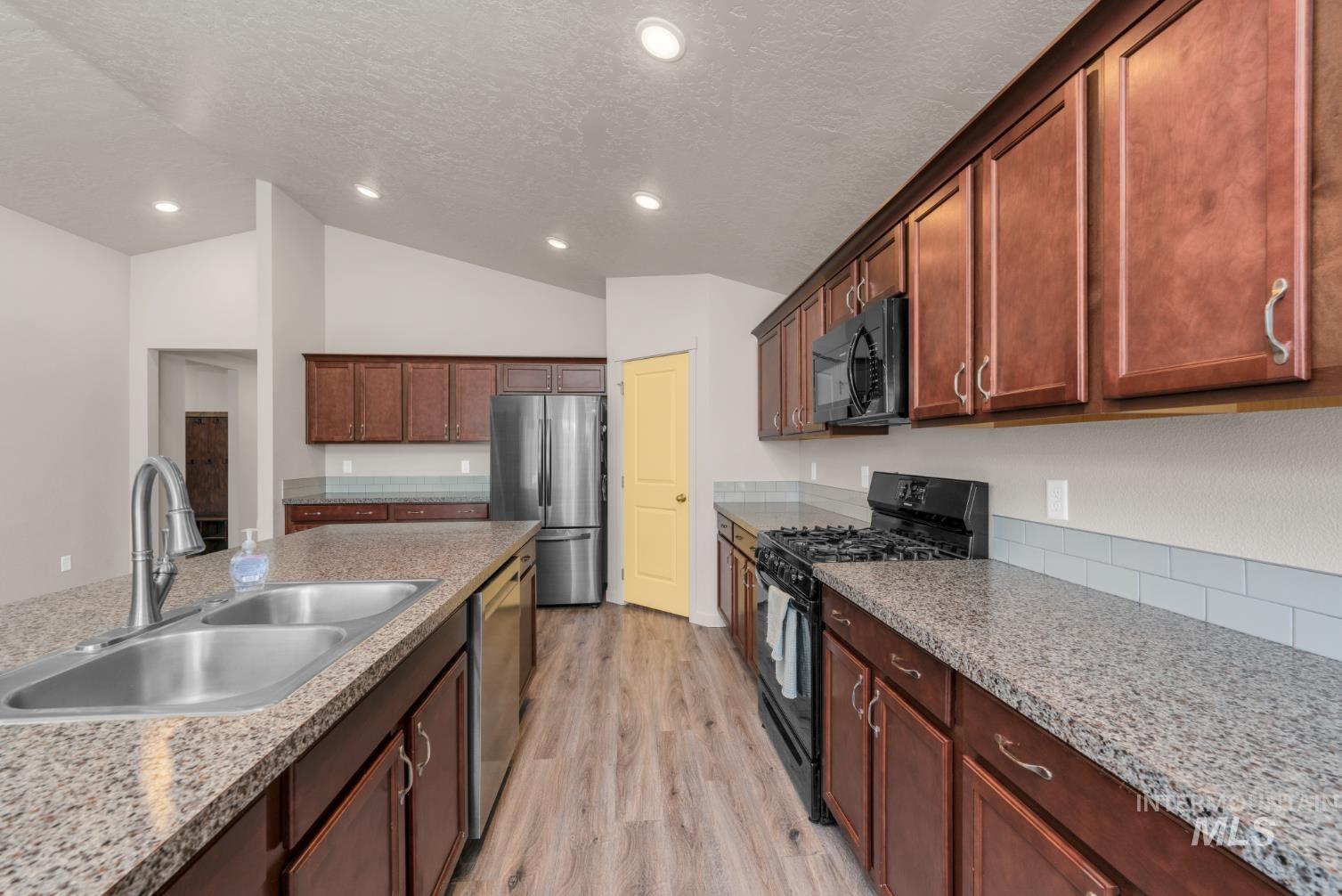 Kitchen with black appliances, plank wood-style floors, a textured and vaulted ceiling