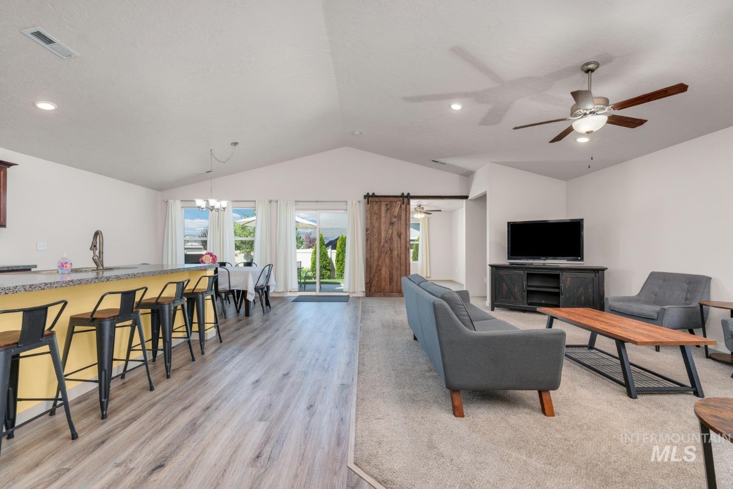 Living area with vaulted ceiling,  barn door, ceiling fan, and Plank flooring