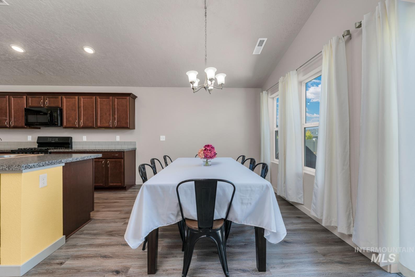 Dining area featuring a chandelier, light plank wood-type flooring, vaulted ceiling, recessed lighting, and a textured ceiling