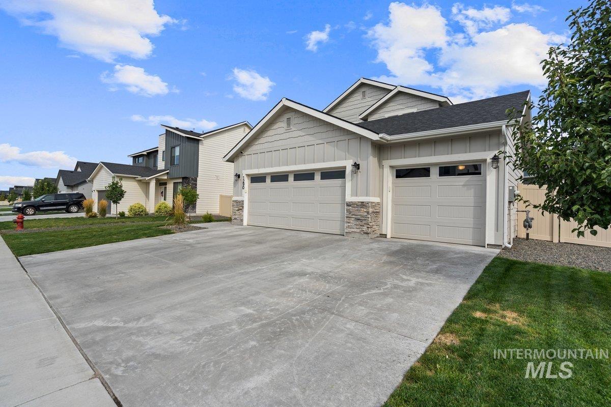View of front of house featuring board and batten siding, stone siding, driveway, a front yard, and an attached garage