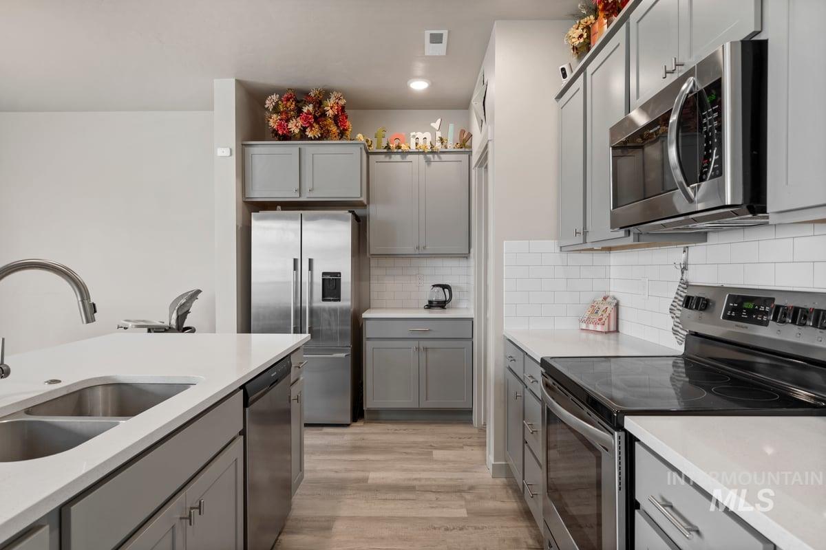 Kitchen with appliances with stainless steel finishes, gray cabinets, decorative backsplash, and light wood finished floors