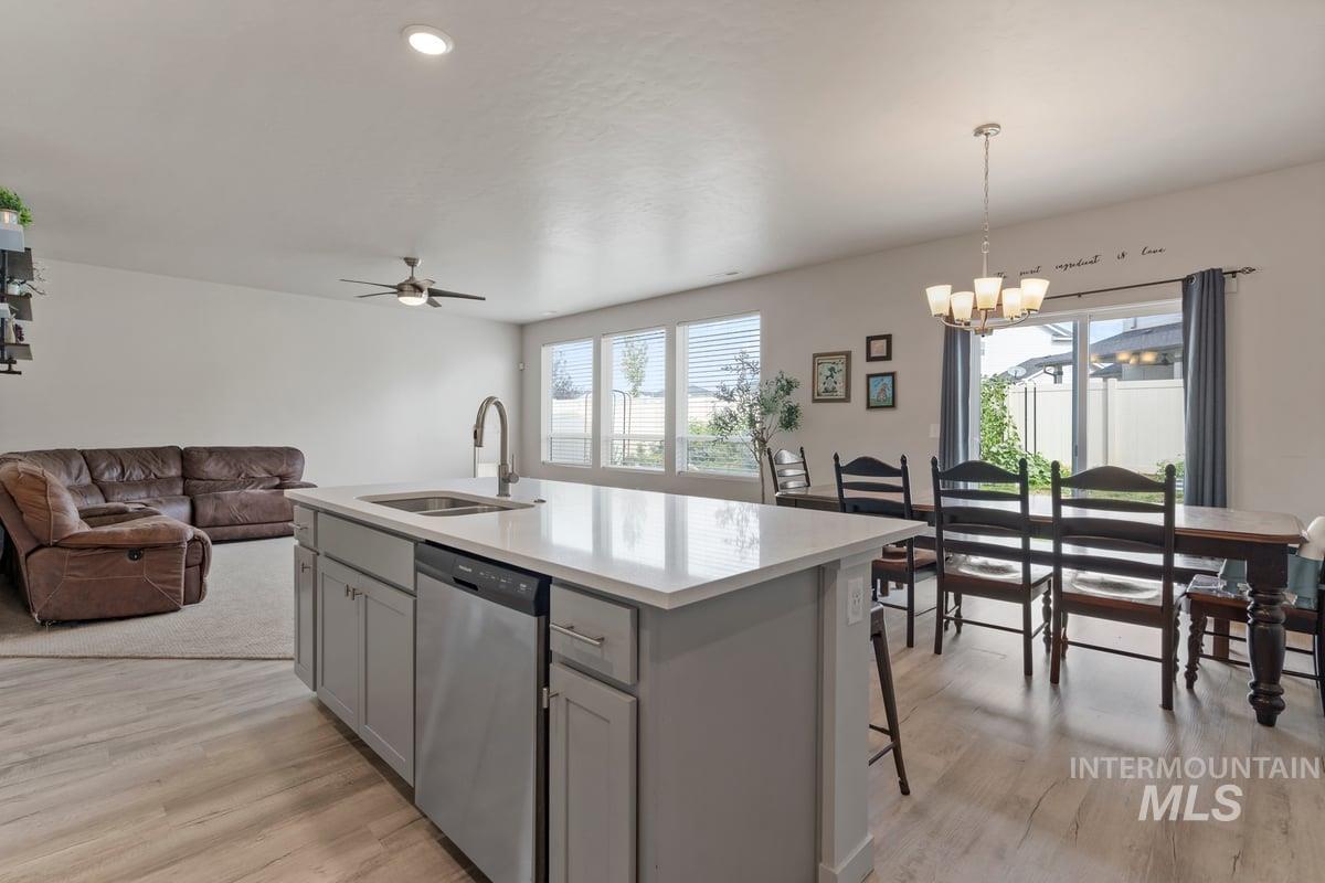 Kitchen featuring open floor plan, stainless steel dishwasher, gray cabinetry, a center island with sink, and plenty of natural light