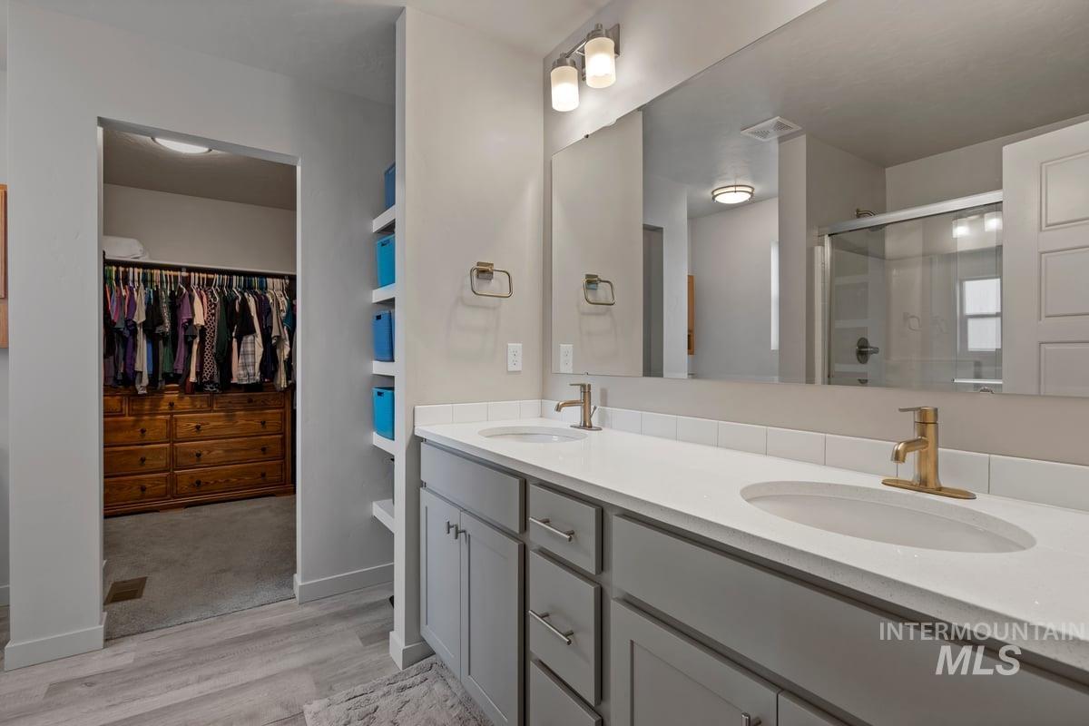 Full bathroom featuring double vanity, a stall shower, light wood-style flooring, and a walk in closet