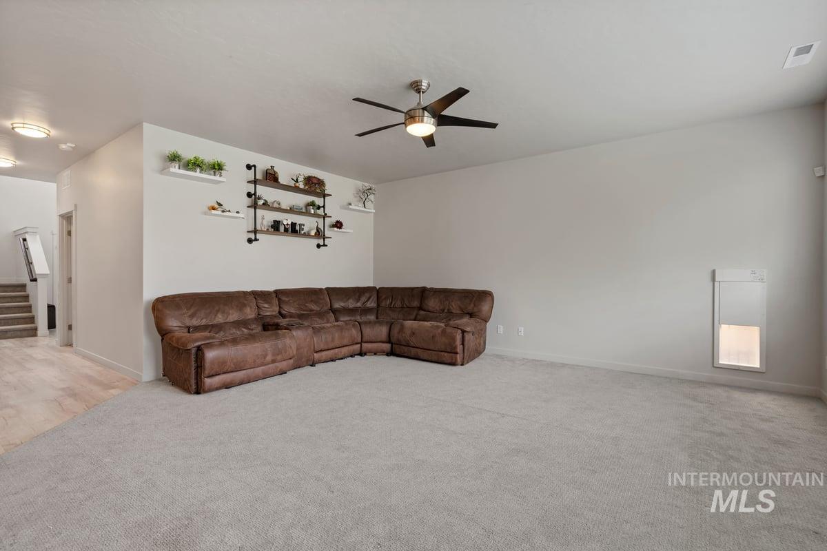 Living room featuring stairs, ceiling fan, and light colored carpet