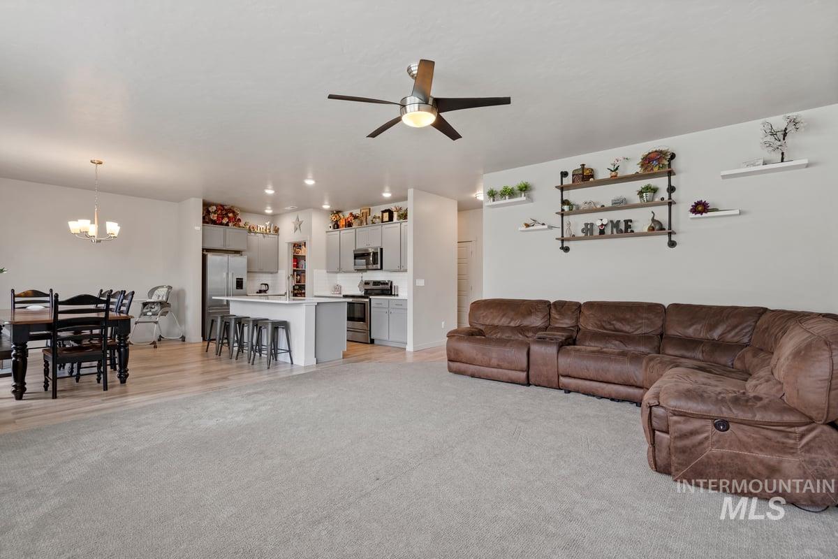 Living room featuring ceiling fan, light carpet, and a chandelier